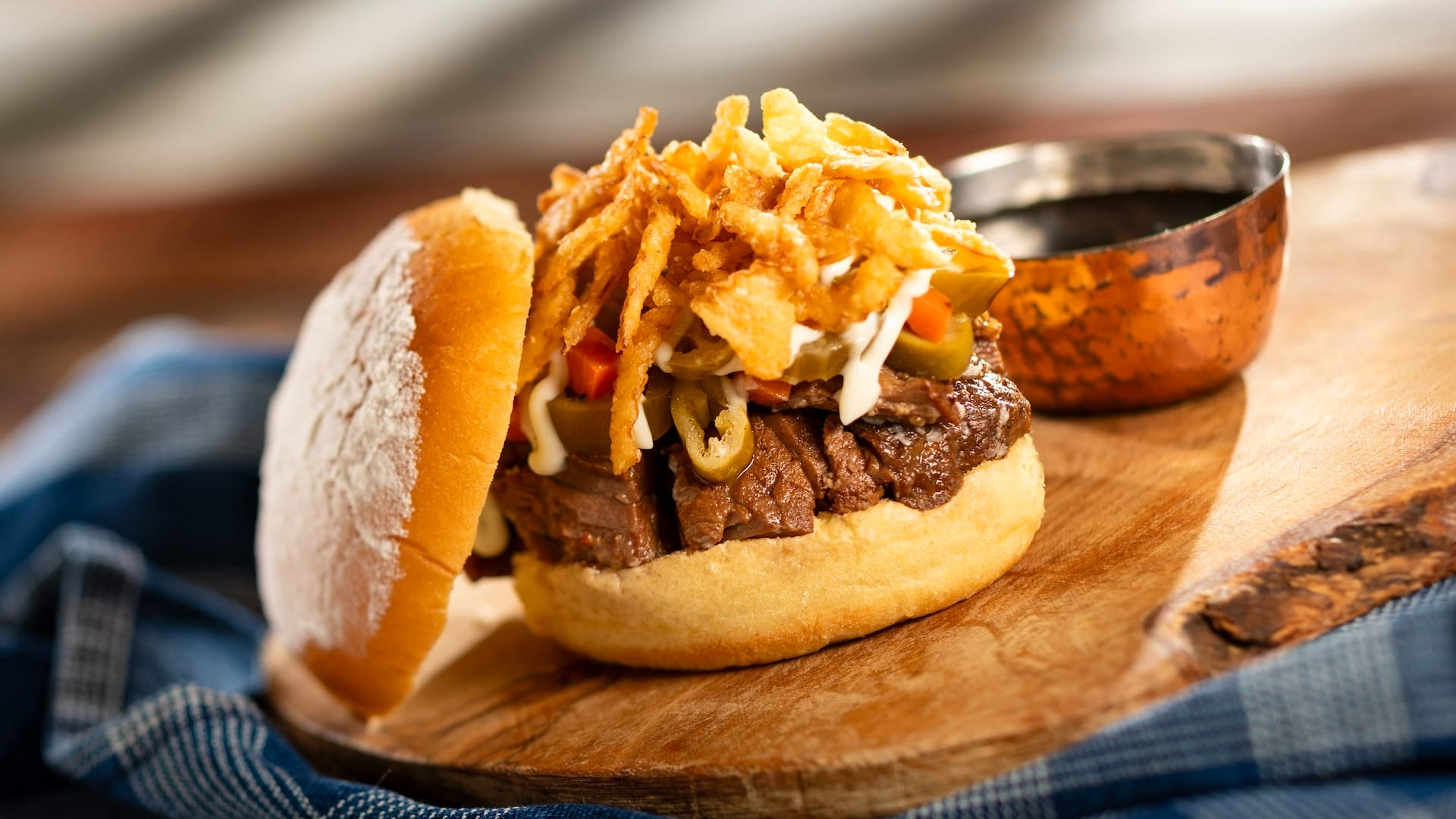 A gourmet burger with sliced beef, olives, and crispy onions—perfect for 2025 menus at the EPCOT Food & Wine Festival.