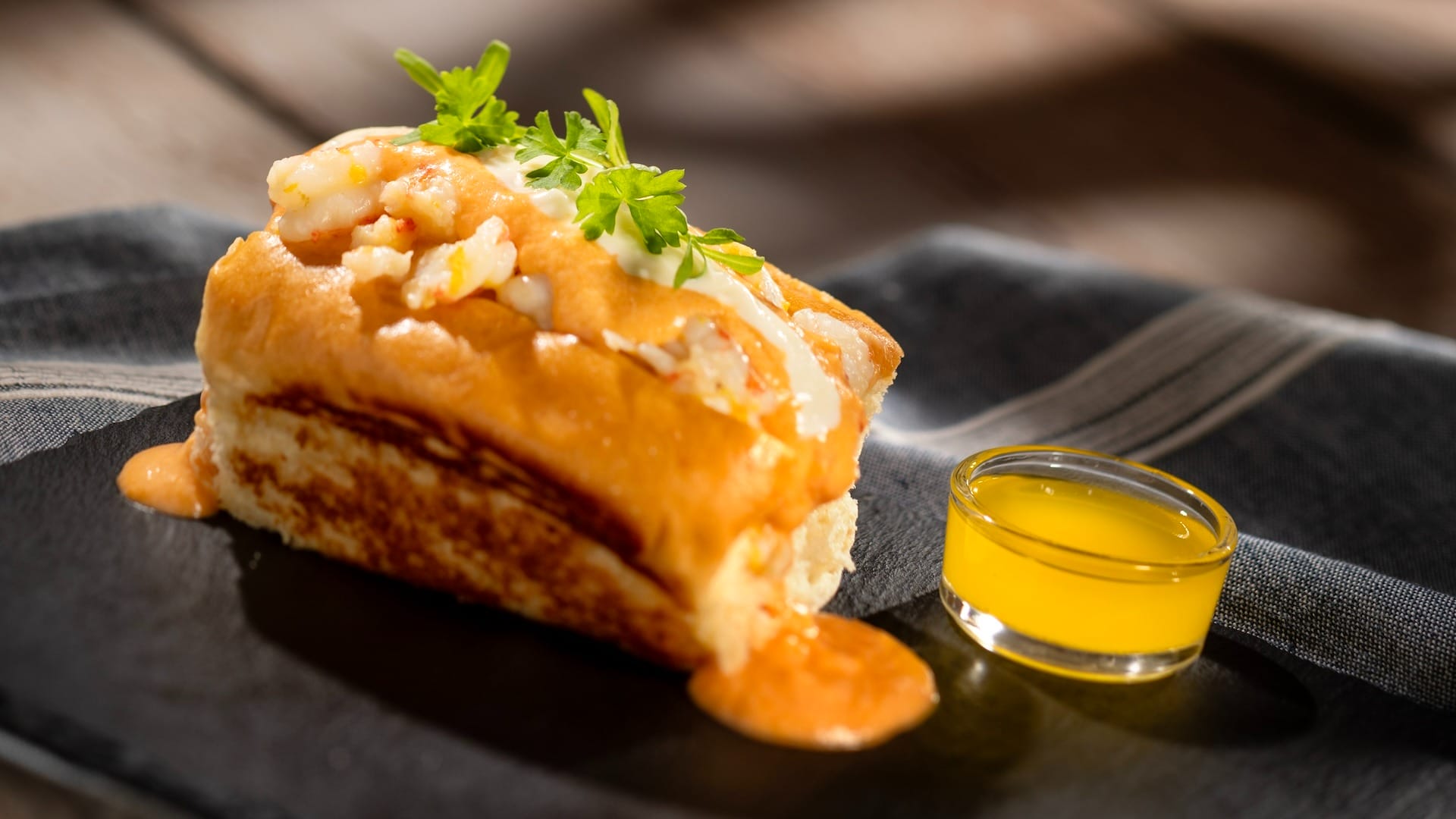 A lobster roll topped with sauce and herbs, featured on 2025 menus at the EPCOT Food & Wine Festival.