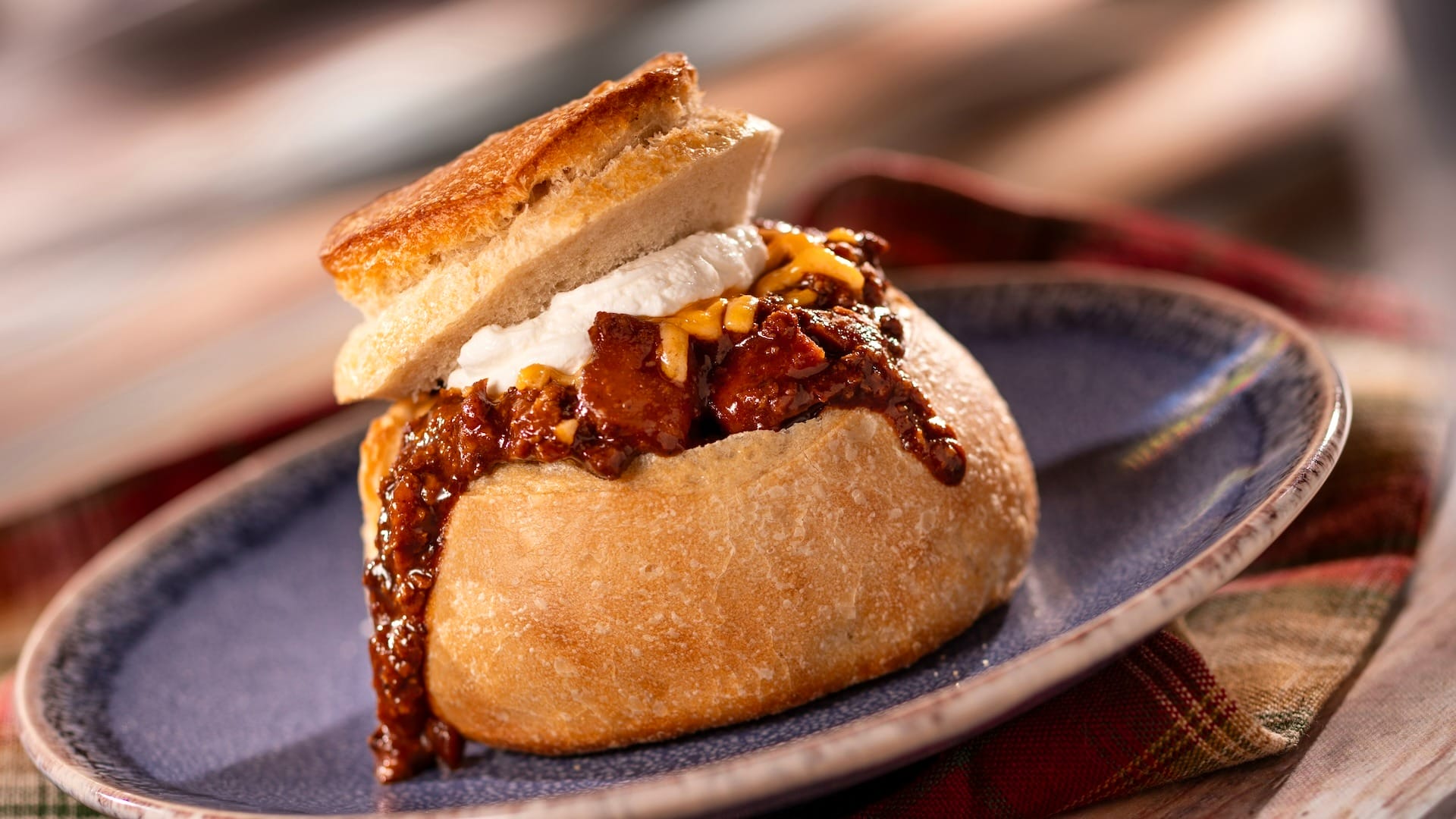 A bread bowl filled with chili, cheese, and sour cream from the 2025 EPCOT Food & Wine Festival sits on a blue plate.