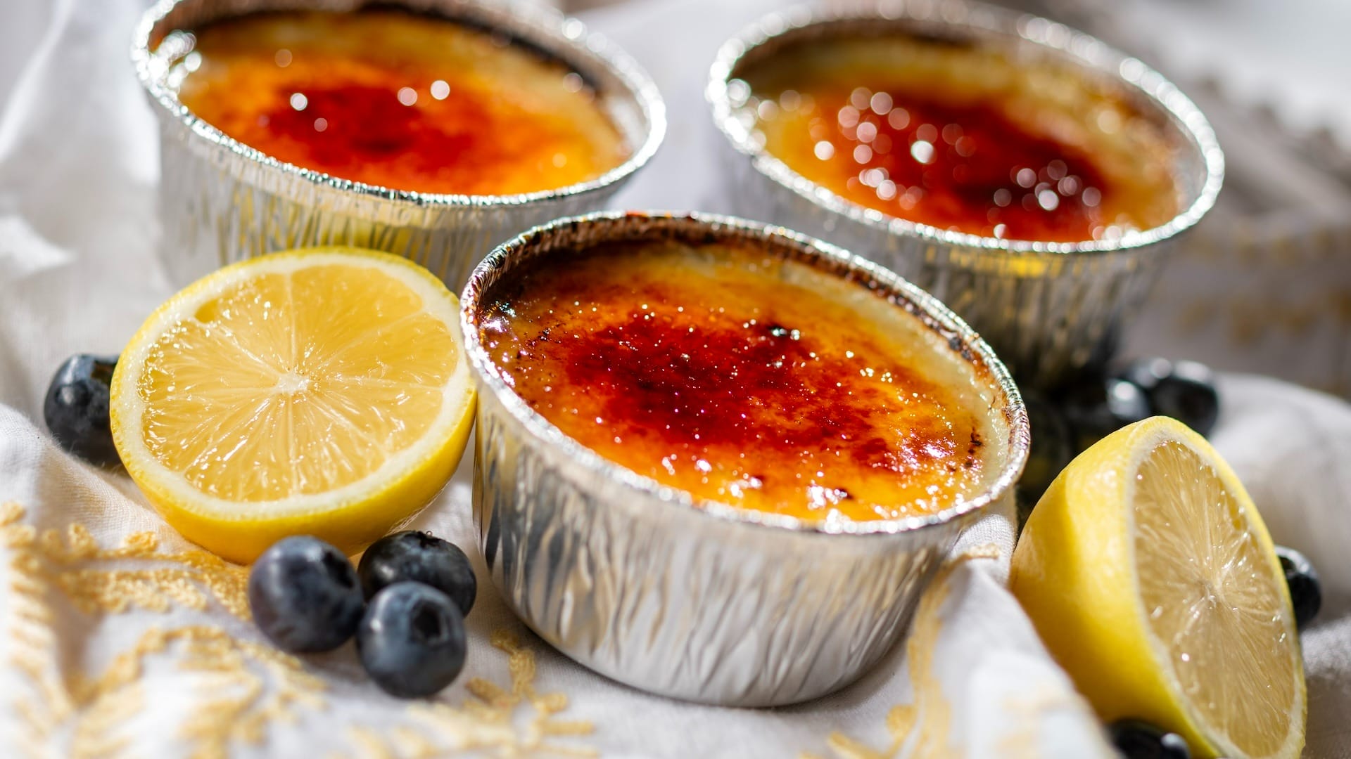 Three crème brûlées in foil cups with caramelized tops, garnished with blueberries—perfect for the EPCOT Food & Wine Festival.