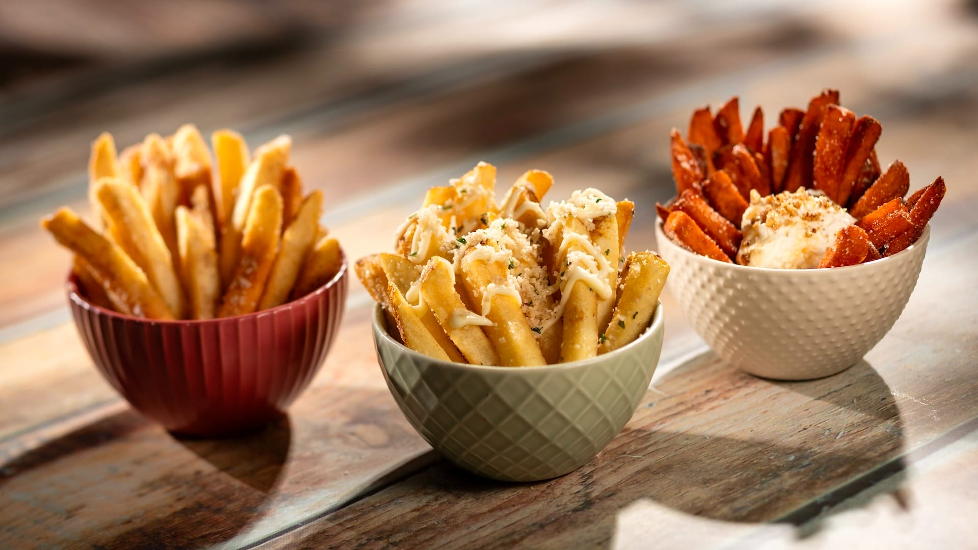 Three bowls of fries on a wooden table, inspired by the EPCOT Food & Wine Festival 2025 menus.