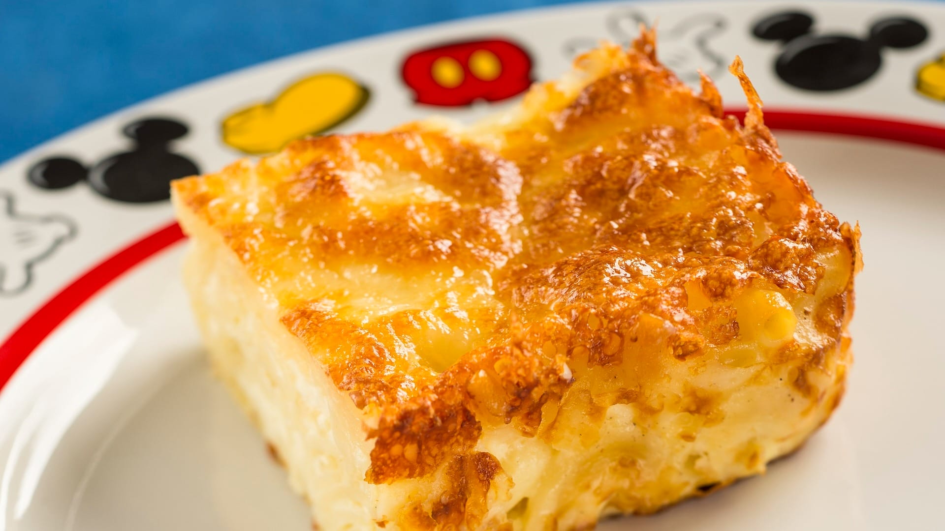 A slice of baked macaroni and cheese on a Mickey plate, perfect for the 2025 menus at EPCOT Food & Wine Festival.