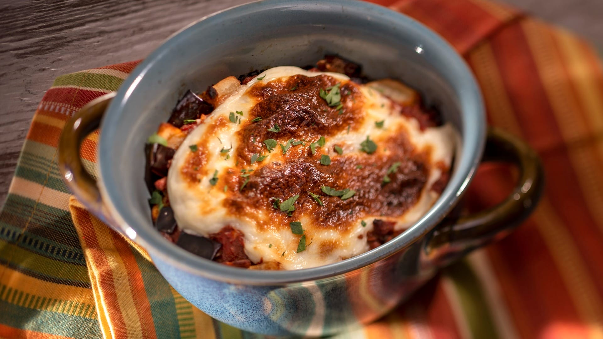 A baked dish topped with melted cheese and herbs in a blue bowl, inspired by EPCOT Food & Wine Festival 2025 menus.