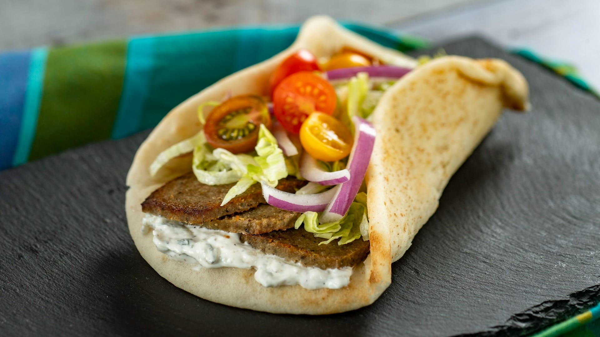 A gyro sandwich from the EPCOT Food & Wine Festival with sliced meat, veggies, and tzatziki on pita bread.