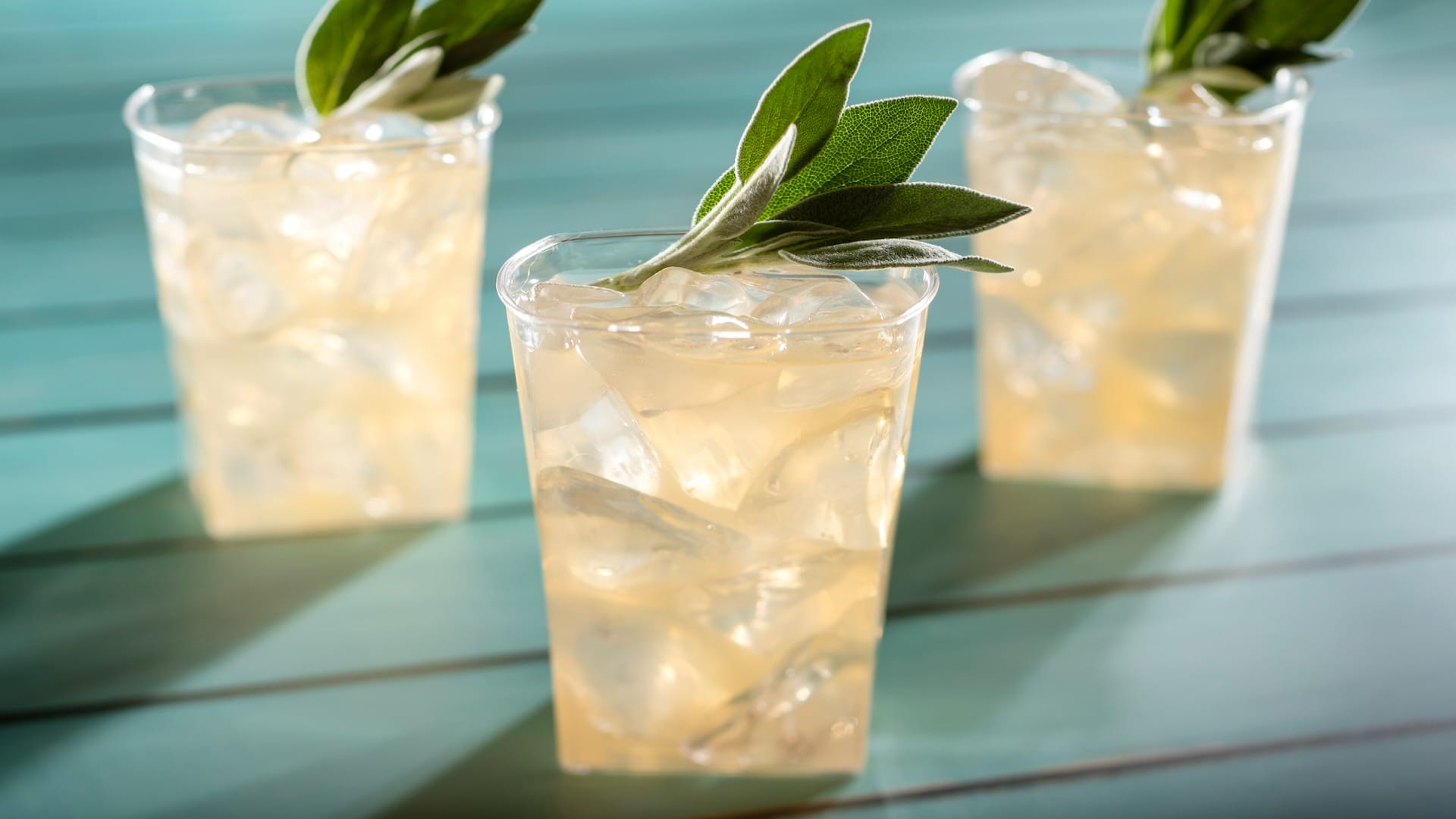 Three iced drinks in clear cups, inspired by EPCOT Food & Wine Festival, on a turquoise wooden surface.