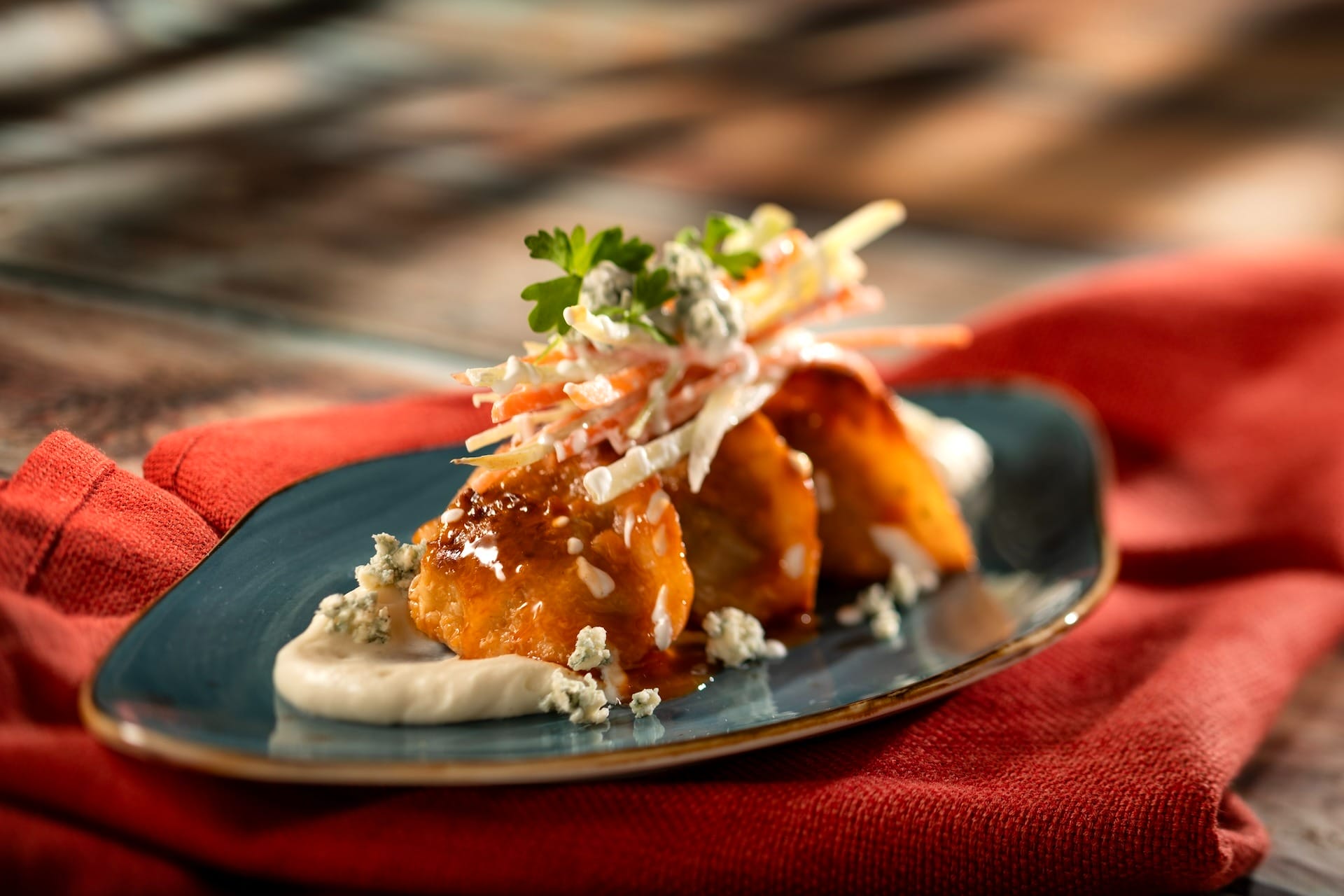 Plated appetizer with glazed bites, creamy sauce, and slaw at an EPCOT Festival food booth, served on a blue dish.