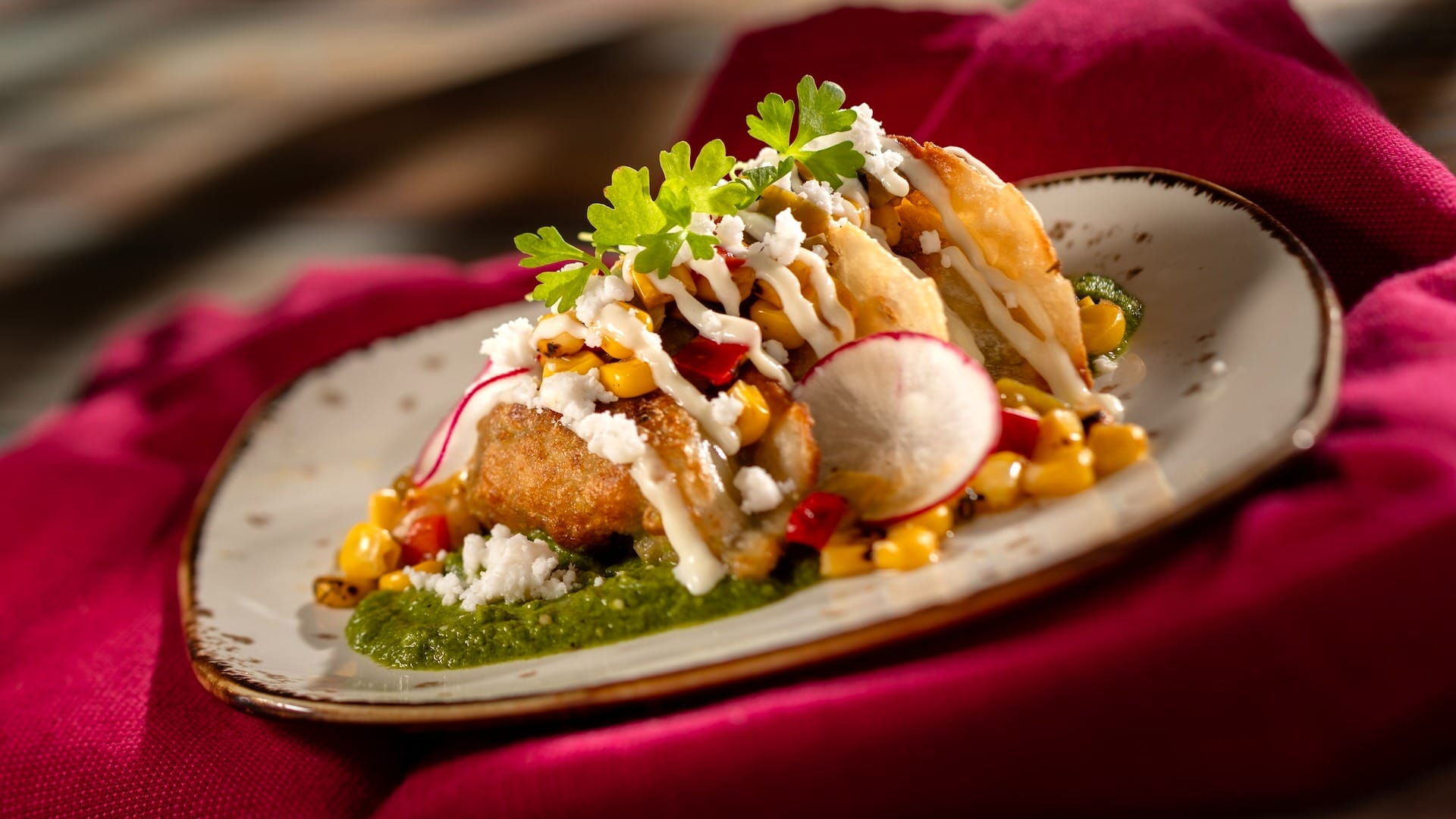 A gourmet dish from a themed food booth at EPCOT Festival, with fried patties, corn, radish, sauce, and herbs.