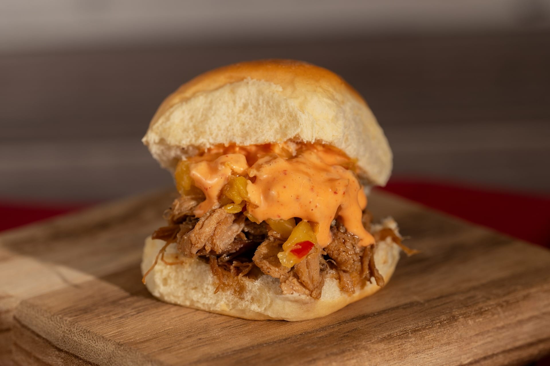 A pulled pork sandwich topped with creamy orange sauce sits on a wooden board at the EPCOT Food & Wine Festival.