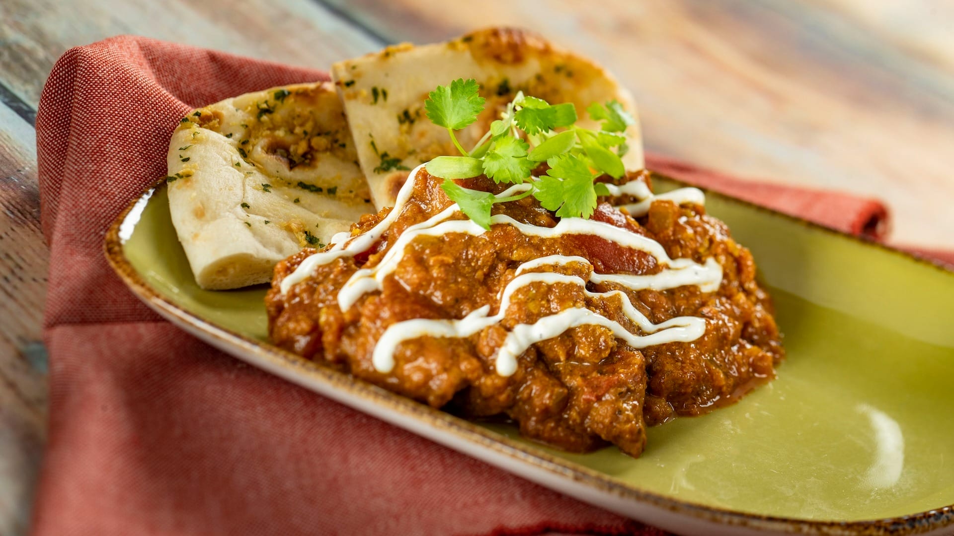 A plate of curry with cream and cilantro, served with naan at the 2025 EPCOT Food & Wine Festival on a green dish.