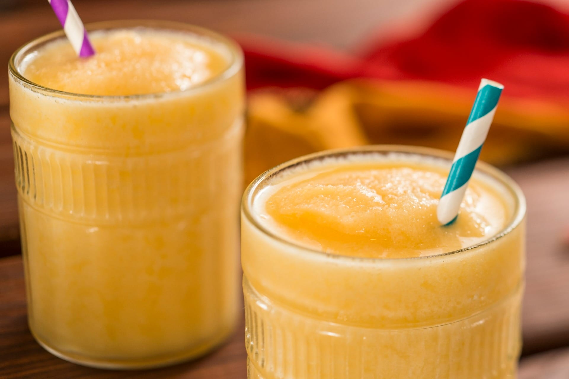 Two glasses of yellow frozen slush drink on a wooden table, perfect for the 2025 menus at the EPCOT Food & Wine Festival.