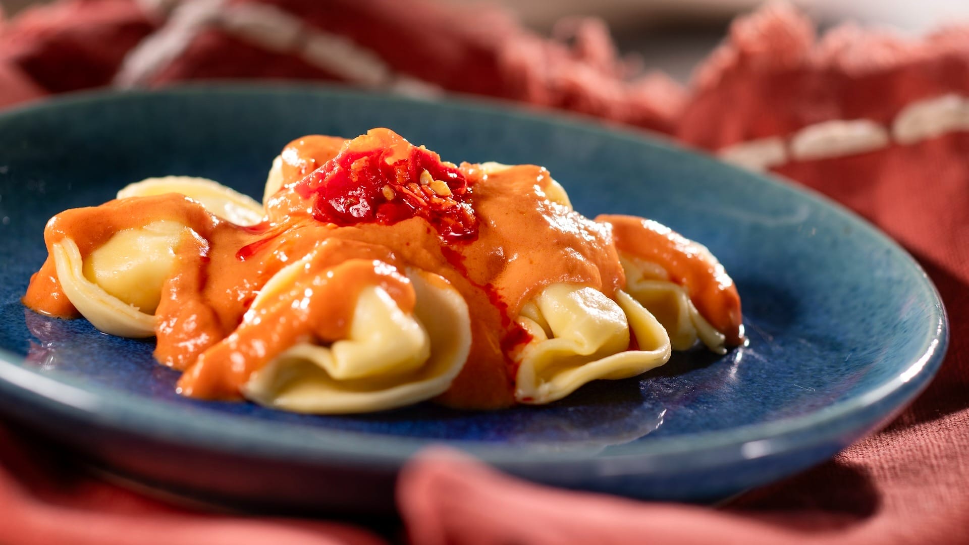 Pasta with creamy tomato sauce, perfect for 2025 menus, on a blue plate against a red cloth background.