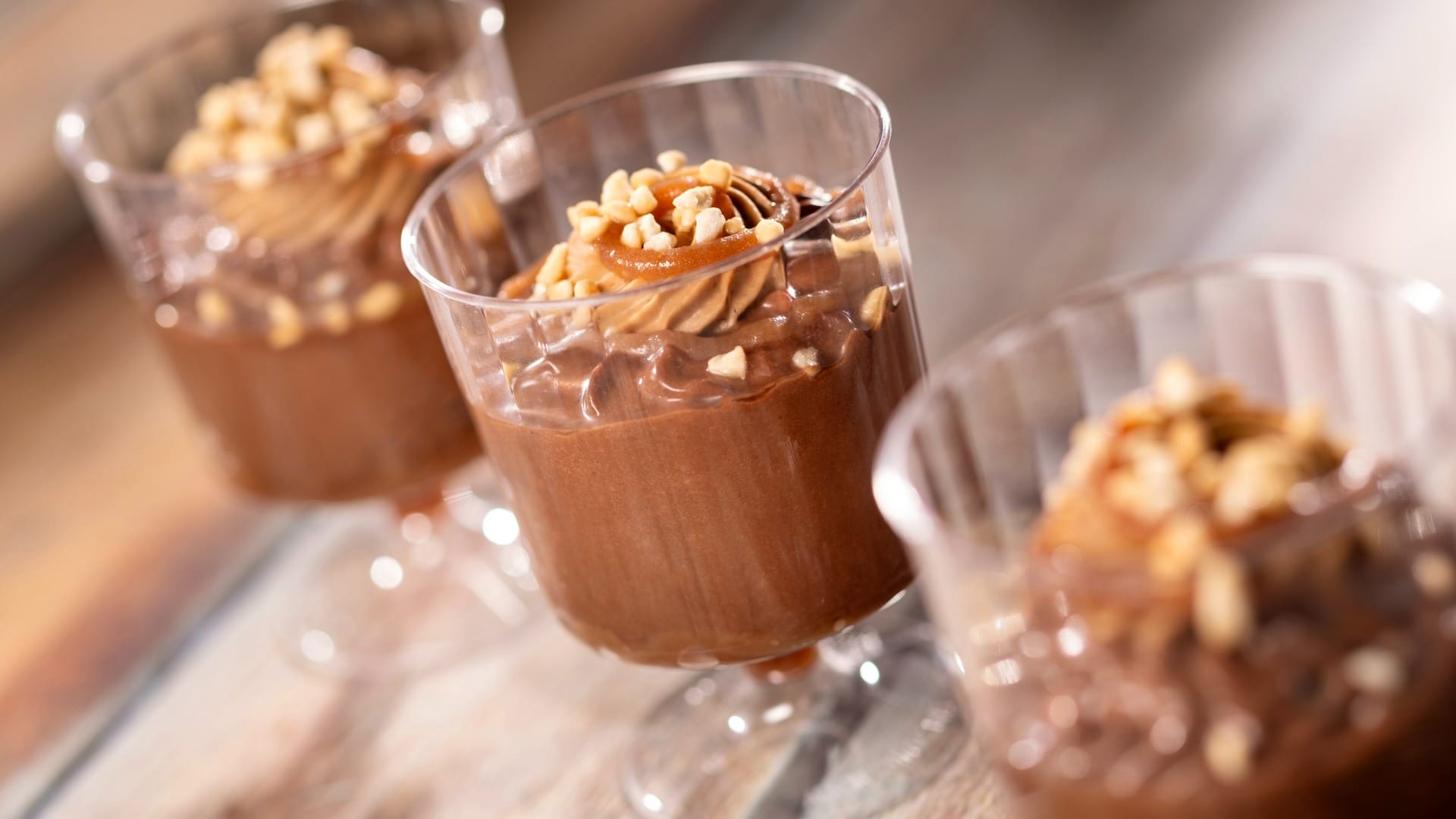 Three glasses of chocolate mousse from the 2025 EPCOT Food & Wine Festival, topped with cream and nuts on a wooden surface.