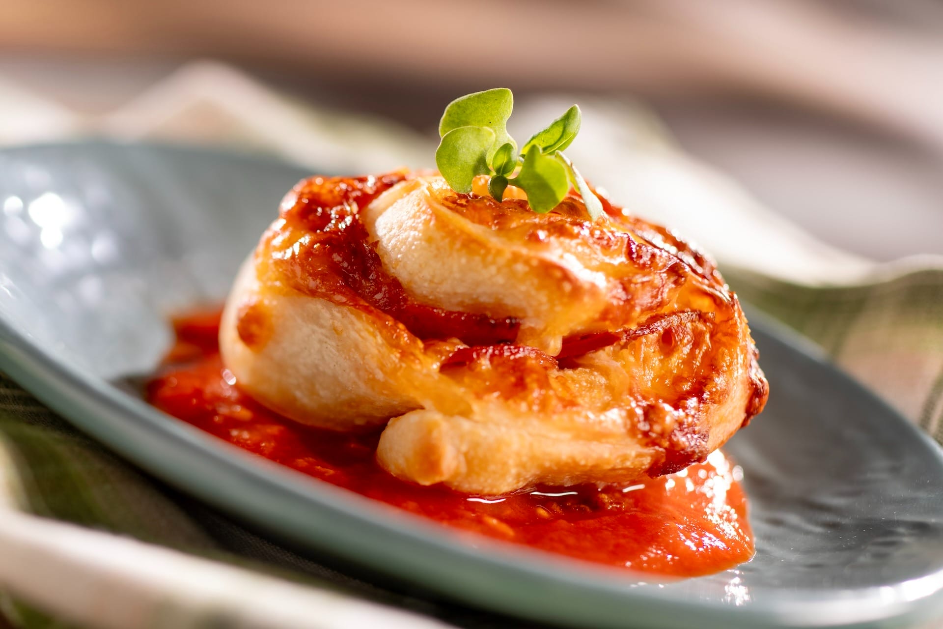 A puff pastry pinwheel with tomato sauce, inspired by EPCOT Food & Wine Festival 2025 menus, served on a gray plate.