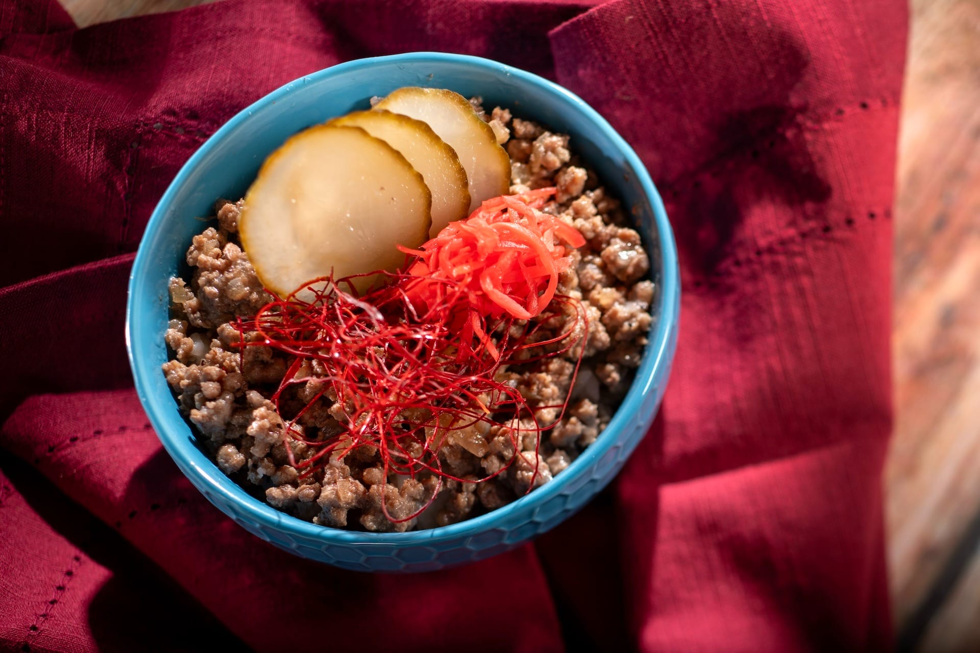 A blue bowl of cooked ground meat with pickles and red ginger—perfect for EPCOT Food & Wine Festival 2025 menus.
