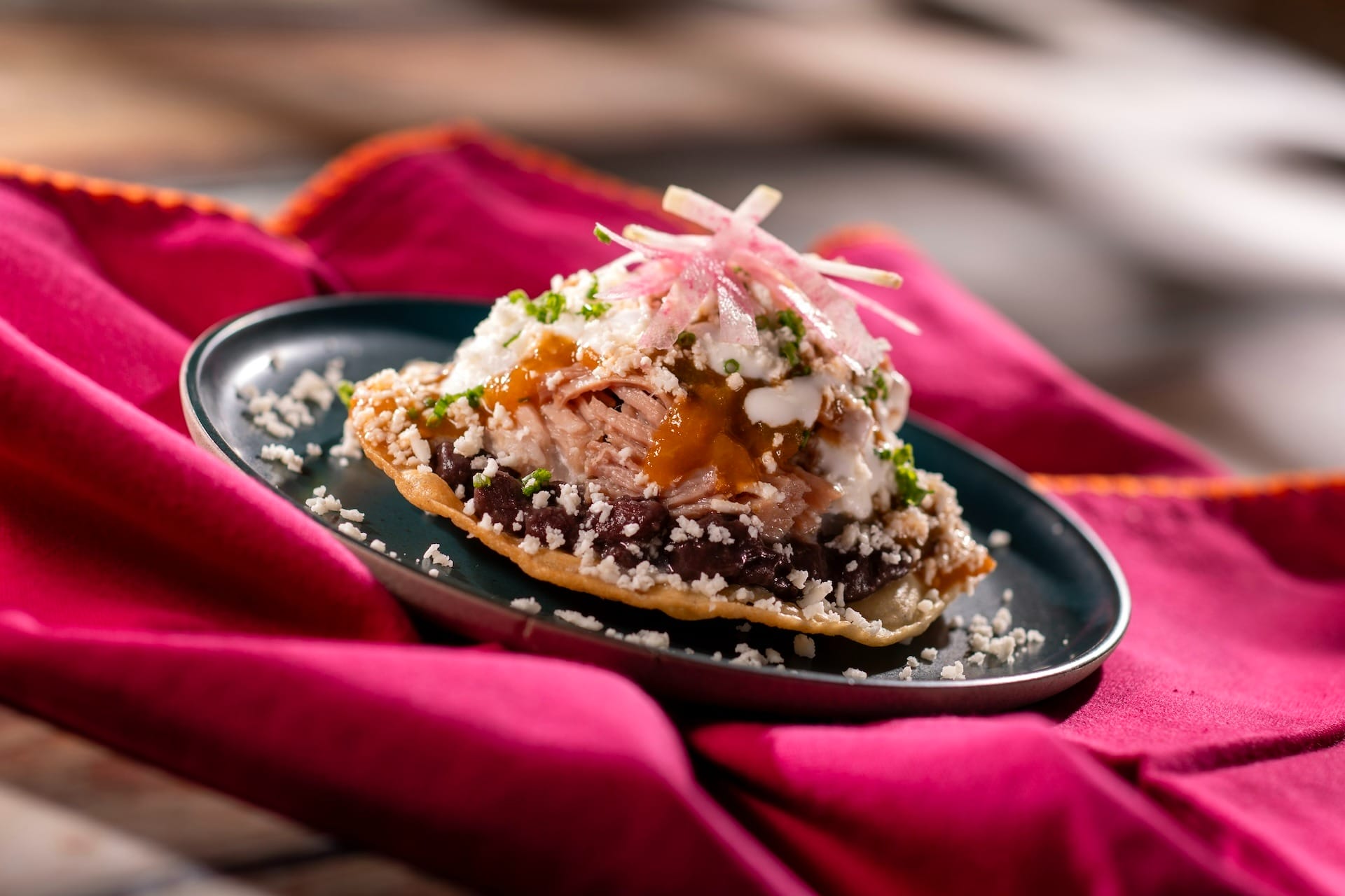 A Mexican tostada from the 2025 EPCOT Food & Wine Festival, topped with beans, meat, cheese, sauce, and fresh radishes.
