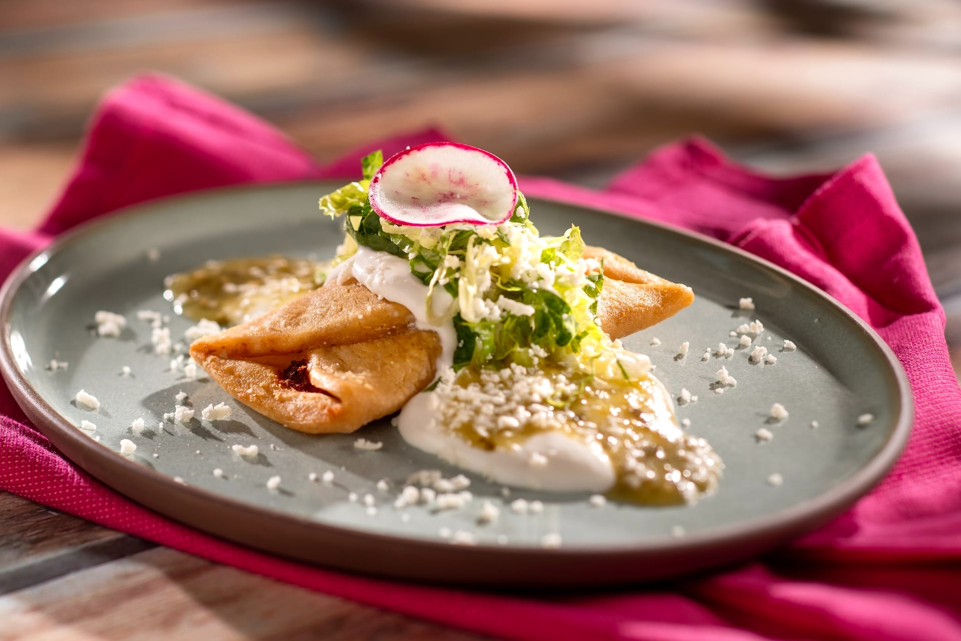 Three empanadas topped with sour cream, lettuce, salsa verde, and cheese from the 2025 menus at the EPCOT Food & Wine Festival.
