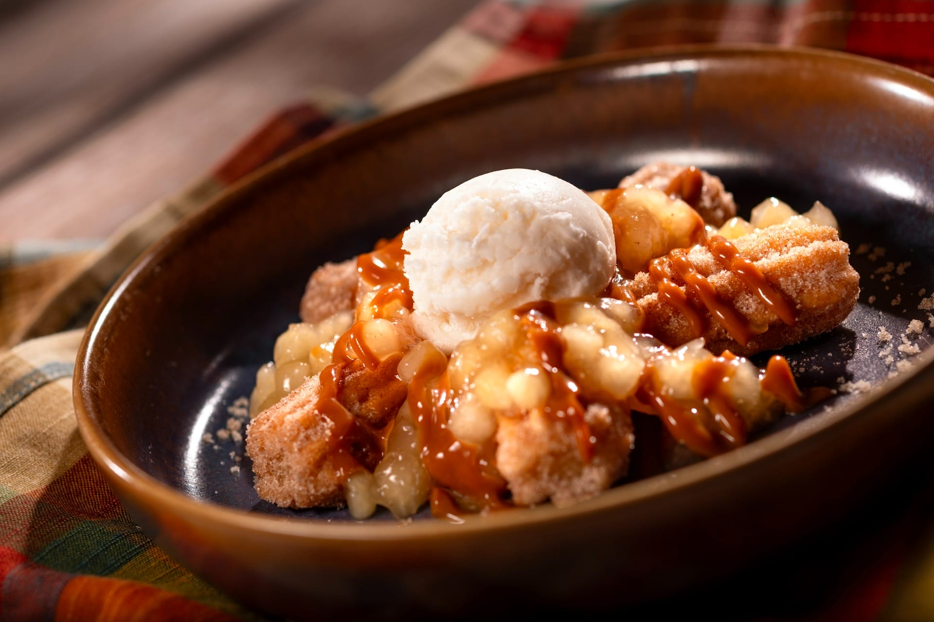 A dessert from the Food & Wine Festival: churros, caramel sauce, apples, and vanilla ice cream on a brown plate.