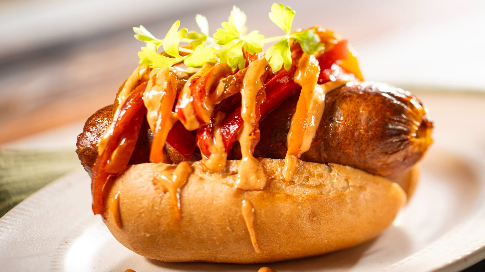 A sausage in a bun topped with sautéed peppers, featured on the 2025 Food & Wine Festival menus.