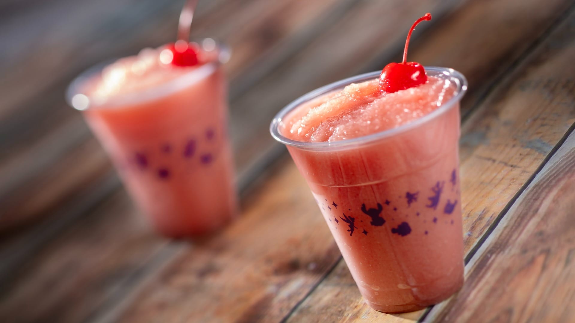 Two frozen pink slush drinks in clear cups at the Food & Wine Festival, each topped with a cherry.