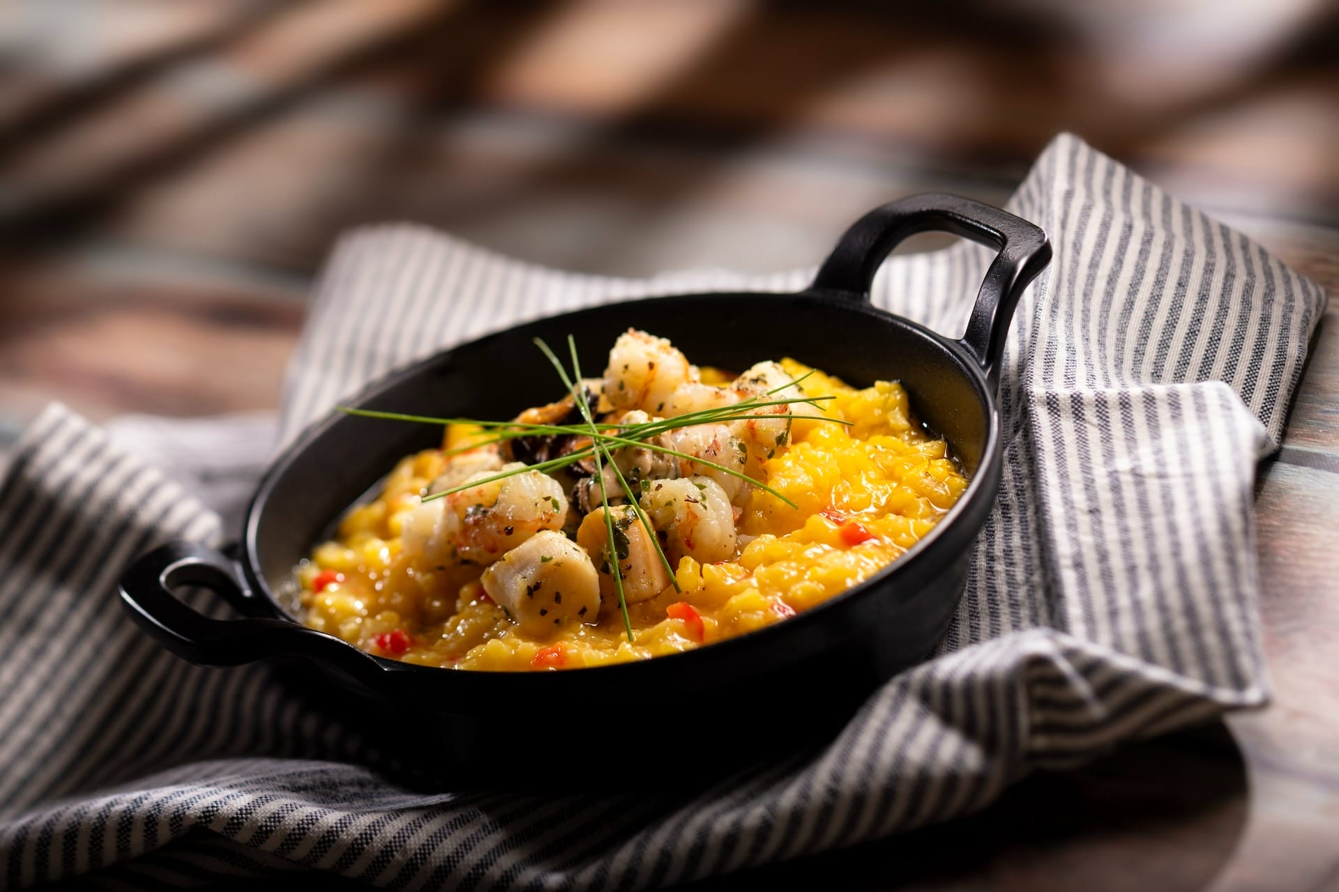 A black dish with creamy risotto, seared scallops, and chives—a highlight on 2025 EPCOT Food & Wine Festival menus.