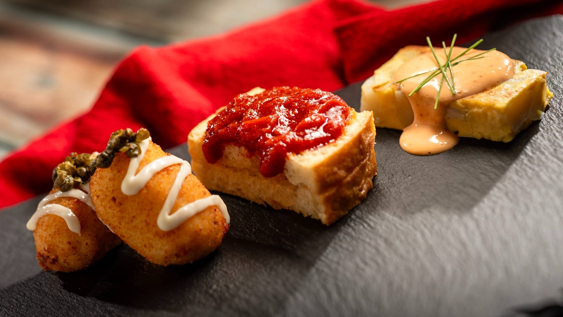 Three gourmet appetizers on a black plate, inspired by the 2025 menus at the EPCOT Food & Wine Festival.