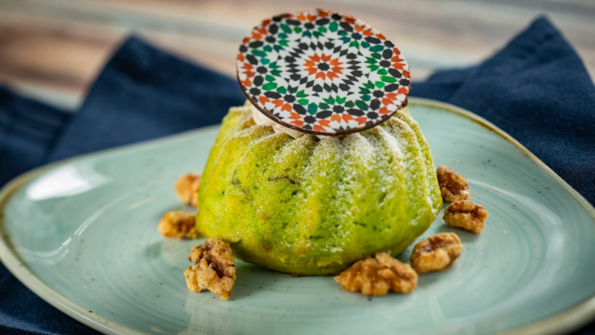 A green dessert with a patterned chocolate disc, walnuts, and light blue plate—perfect for the 2025 menus at EPCOT Food & Wine Festival.