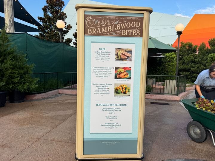 Brown and blue Bramblewood Bites menu sign at Epcot showcases New Food & Wine options, outdoors near greenery.
