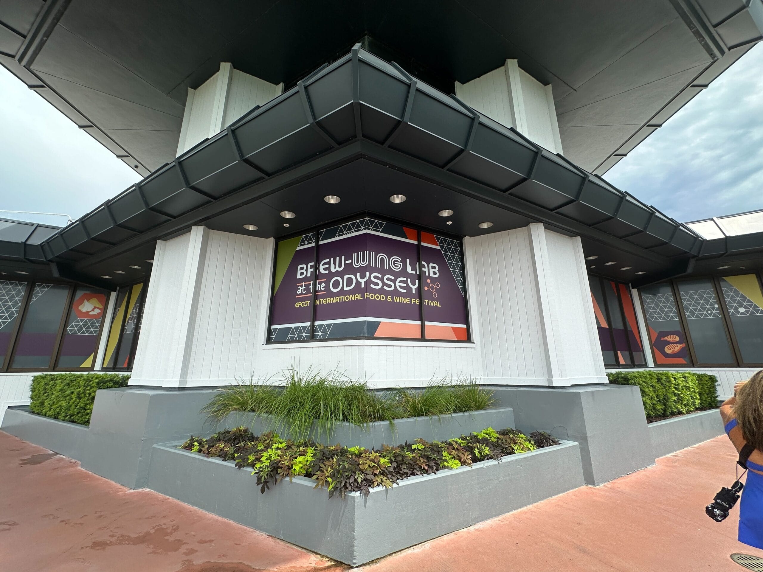 Exterior of Brew-Wing Lab at the Odyssey with a large sign and surrounding plants at the building’s base.