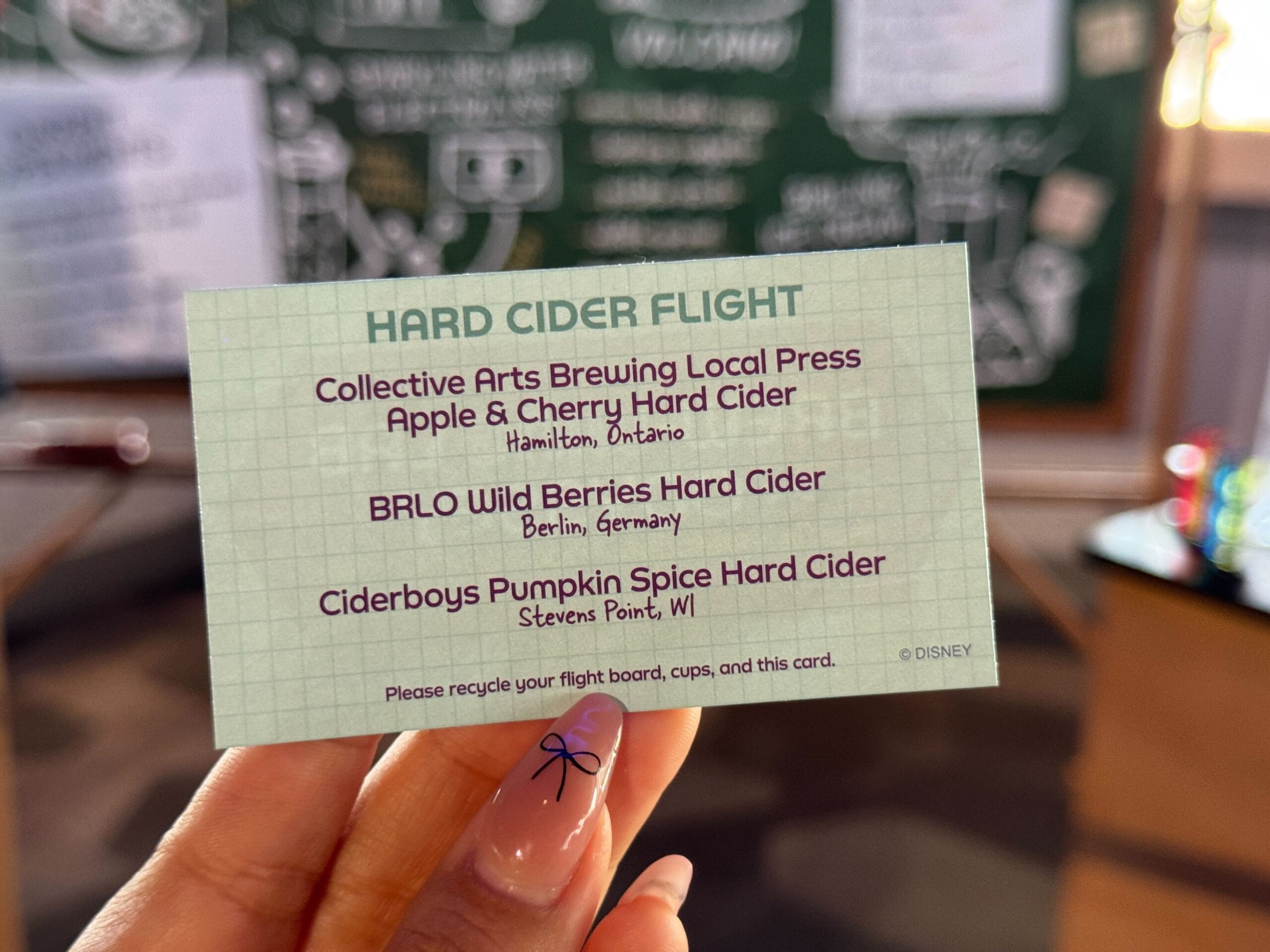 Hand with a card listing three hard ciders for a New Food & Wine cider flight tasting from Canada, Germany, and Wisconsin.