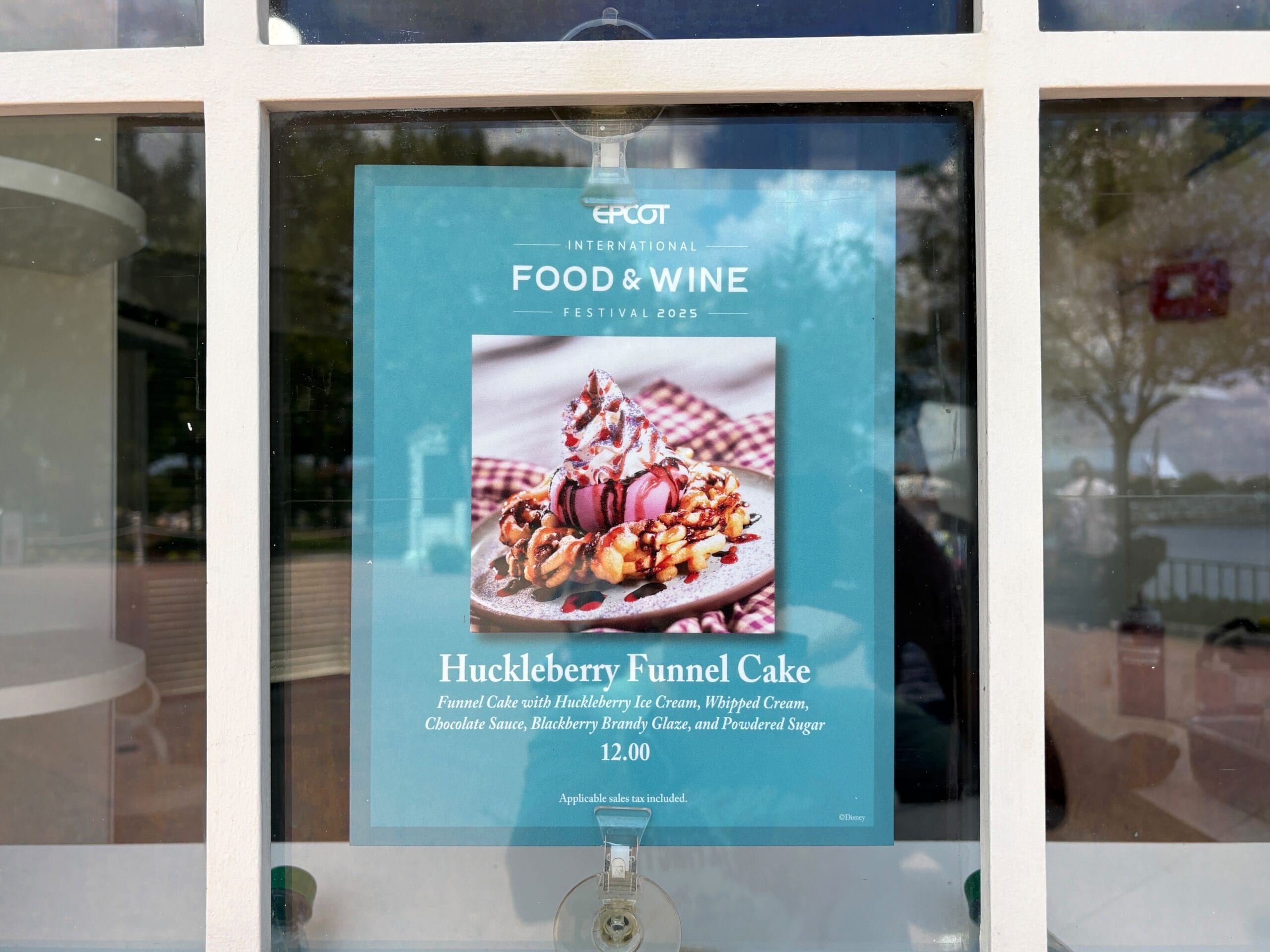 A sign advertises New Food & Wine Huckleberry Funnel Cake topped with ice cream, whipped cream, and berries at Epcot.