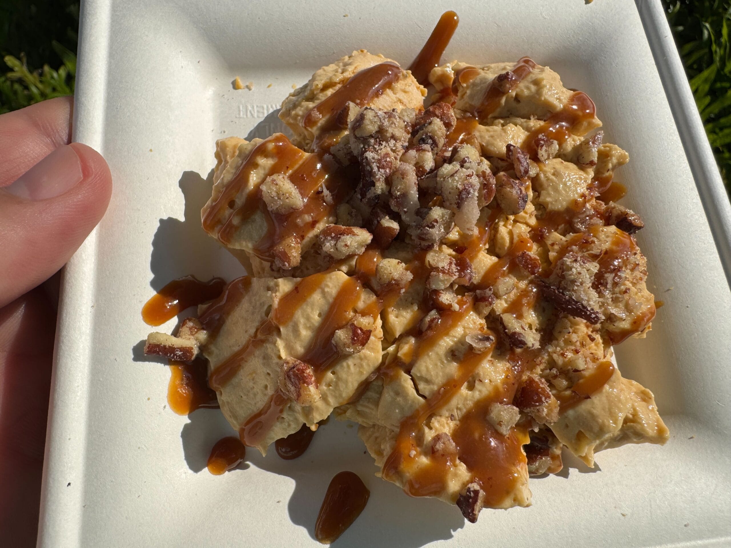 A hand holds a plate of dessert topped with chopped nuts and drizzled caramel, featured at New Food & Wine.