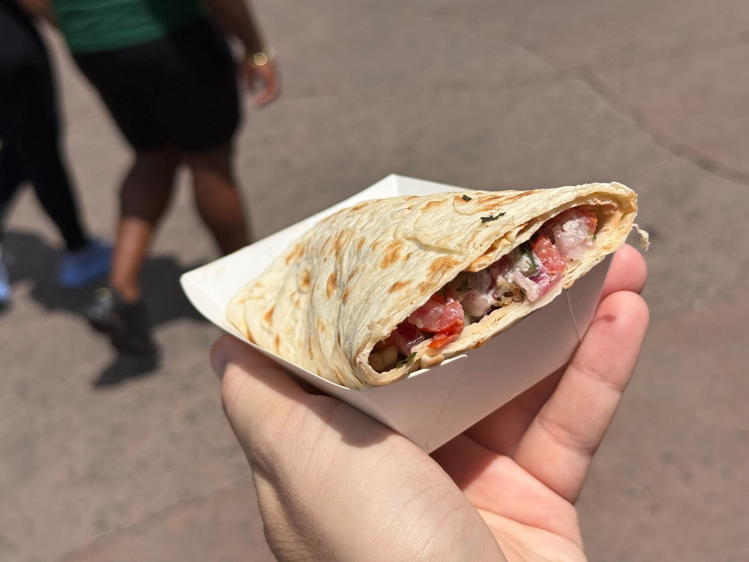A hand holding a filled flatbread wrap in a paper tray, perfect for enjoying at the Food & Wine festival.