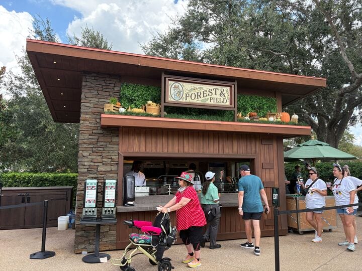 Outdoor food kiosk "Forest & Field" serves New Food & Wine delights, with people ordering amid lush greenery.