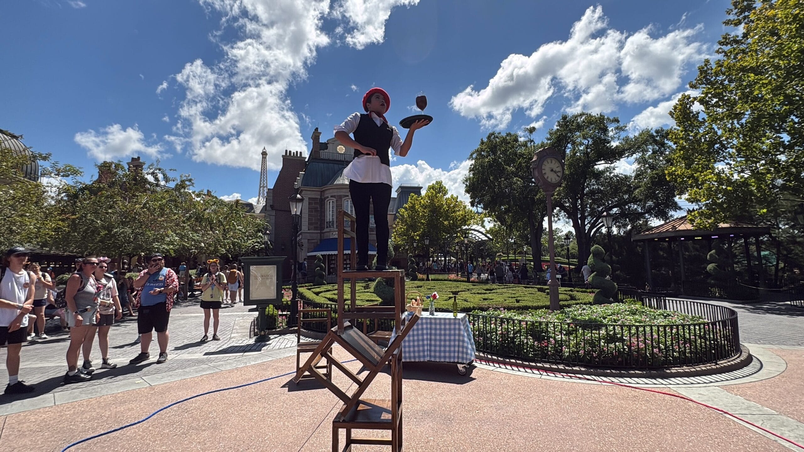 An Acrobatic Show unfolds as a street performer balances on stacked chairs, delighting crowds in a sunny park at EPCOT.