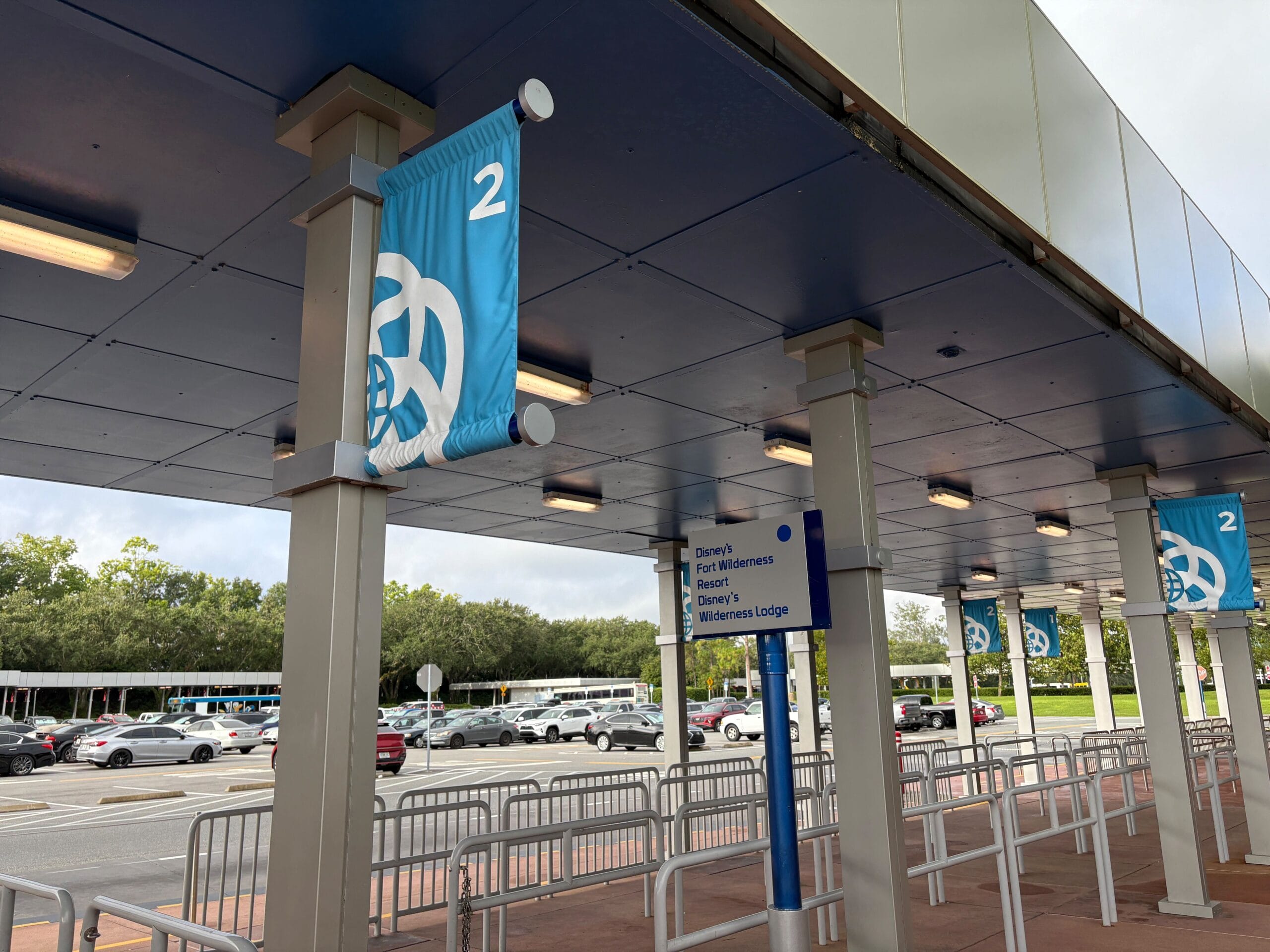 Blue banners with a white EPCOT logo and the number 2 mark the bus stop expansion, with signs and cars in the background.