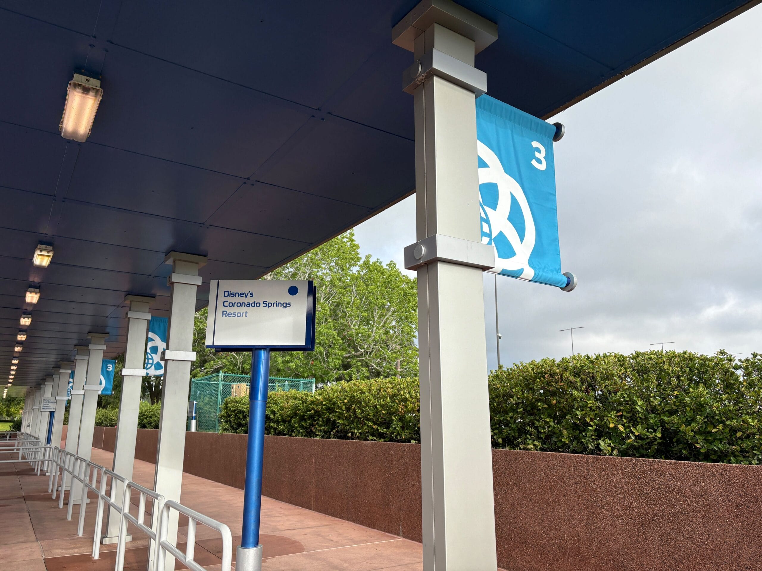 Covered EPCOT Bus Stop for Disney’s Coronado Springs Resort, with a blue “3” banner and greenery in the background.