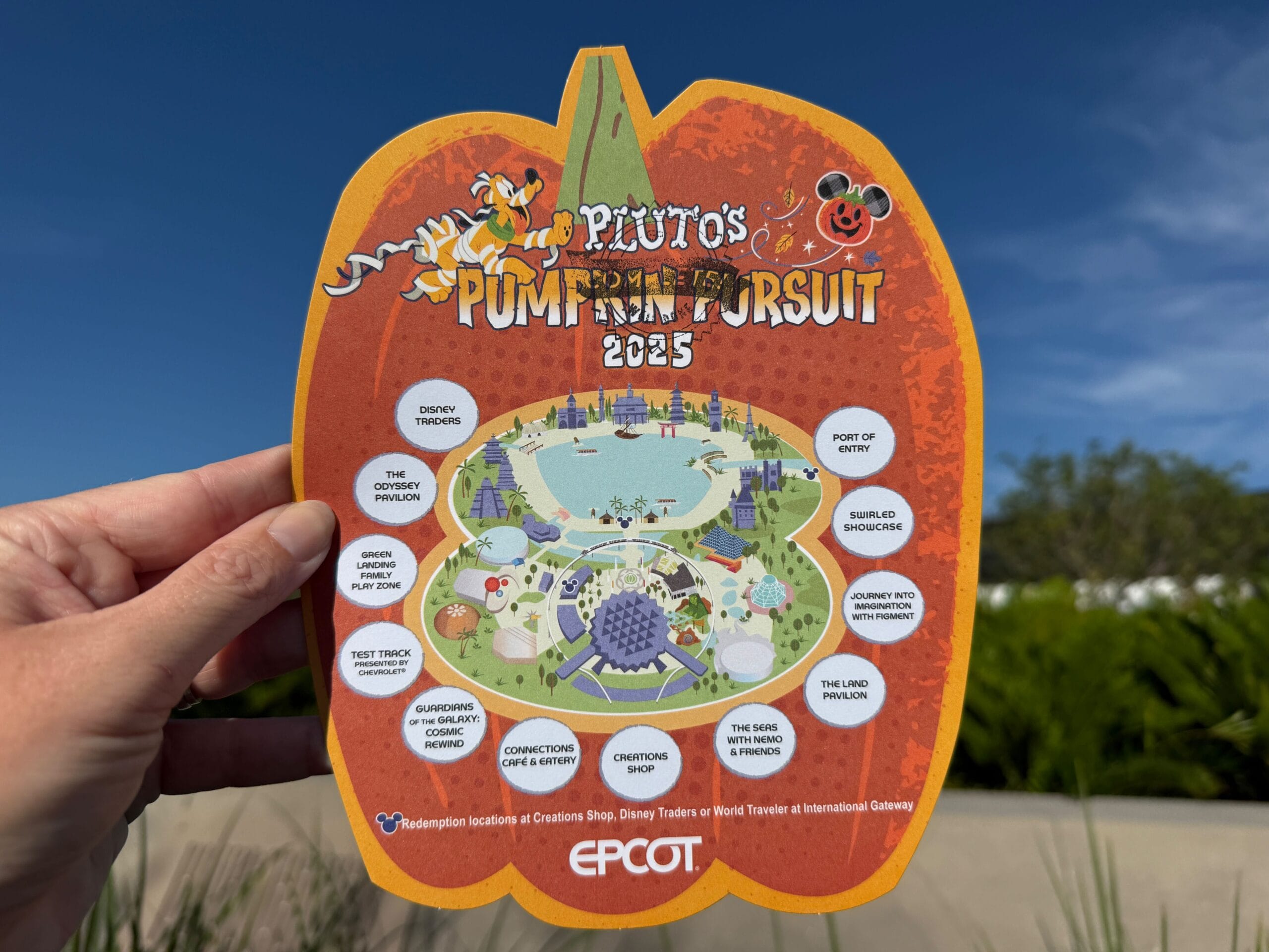 A hand holds up a Pluto's Pumpkin Pursuit event map at Disney World EPCOT, highlighting attraction icons for 2025.