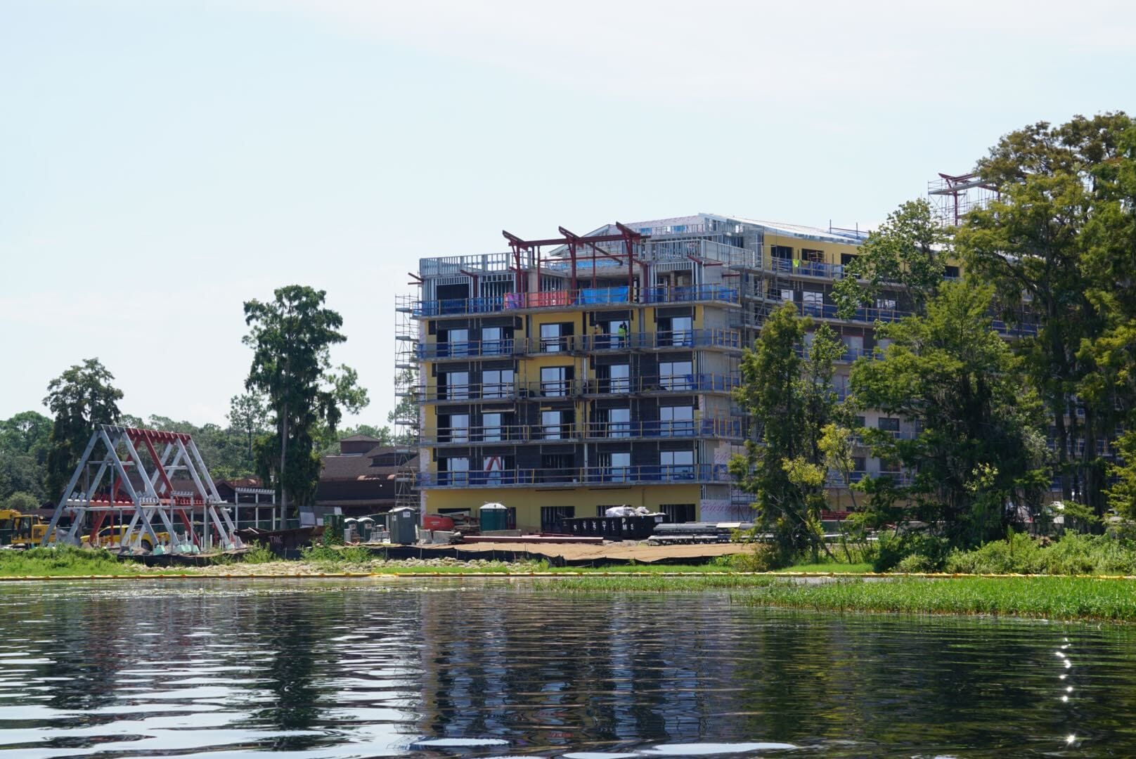 A mid-rise building under construction stands near a lake, part of the latest Lakeshore Update, surrounded by trees.