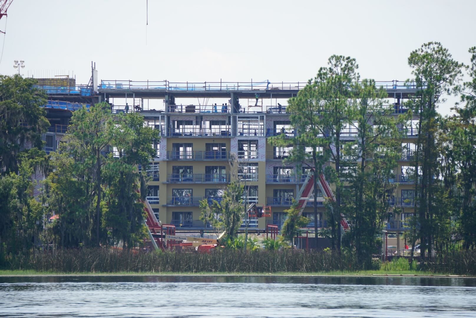 A multi-story building under construction, partially obscured by trees, with a lake in the foreground—Lakeshore Update.