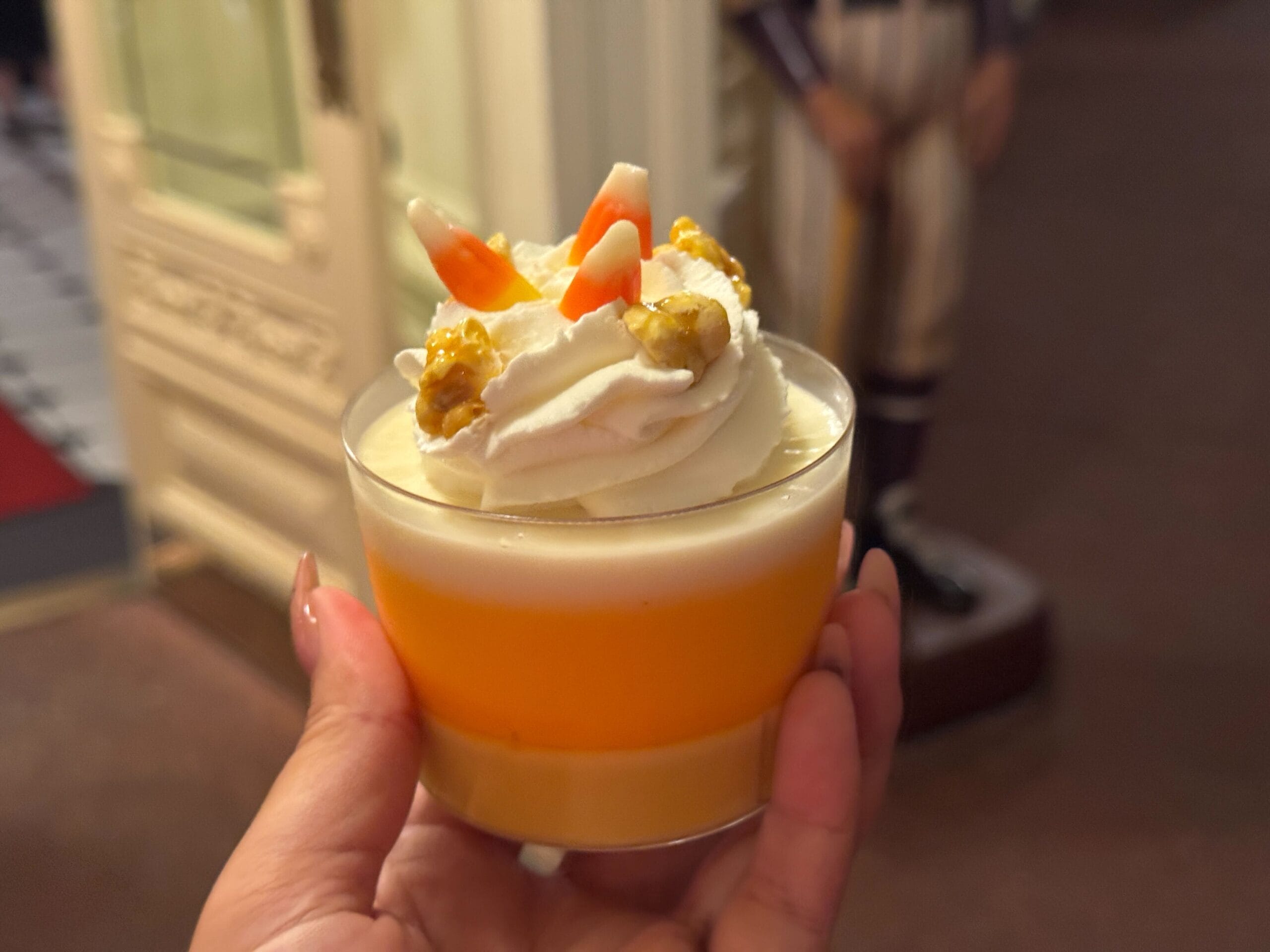 A hand holds a layered dessert topped with whipped cream, candy corn, and walnuts at Mickey's Not So Scary Halloween Party.