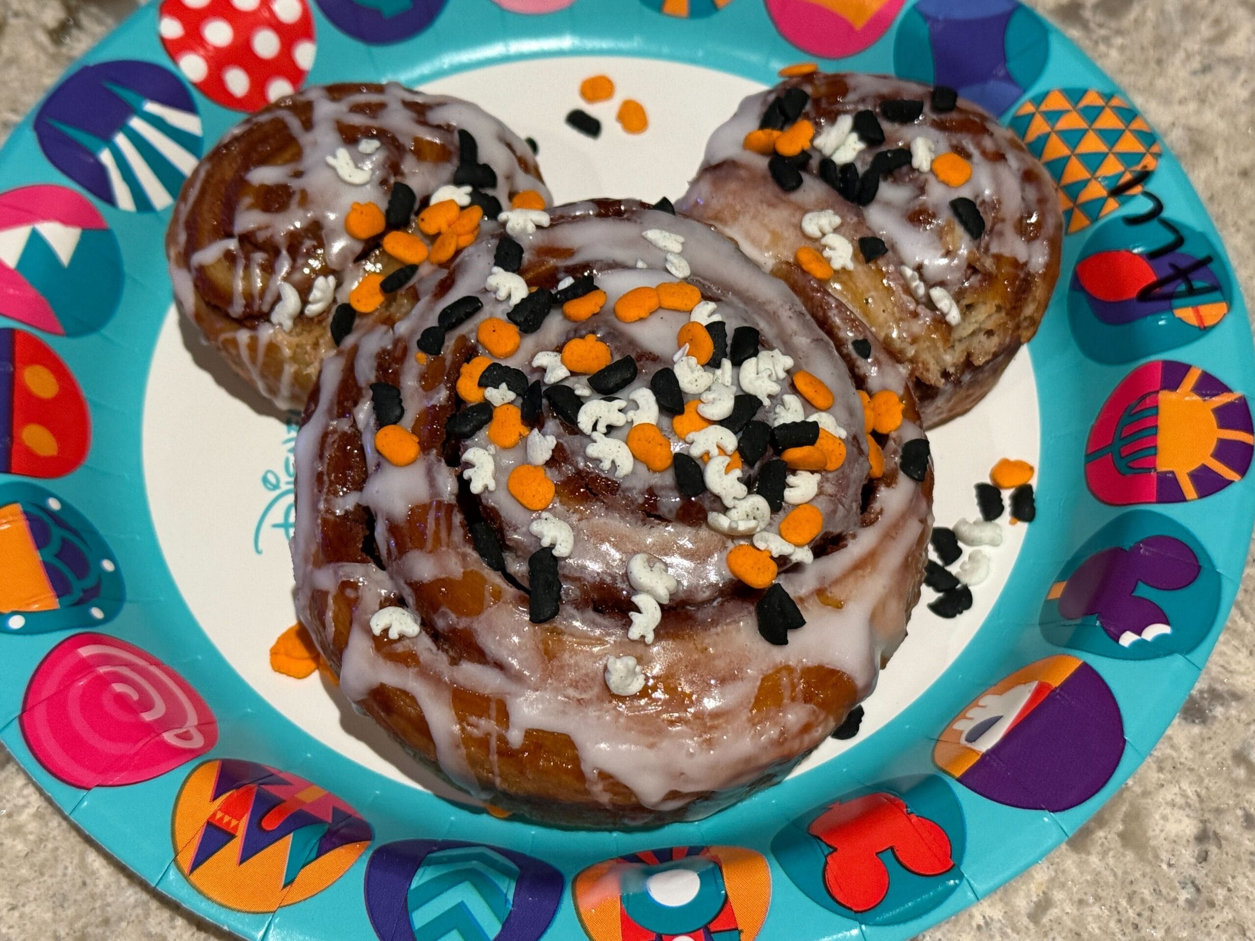 A Mickey Mouse-shaped cinnamon roll with icing and Halloween sprinkles featured in our Mickey's Not So Scary Halloween Party food reviews.