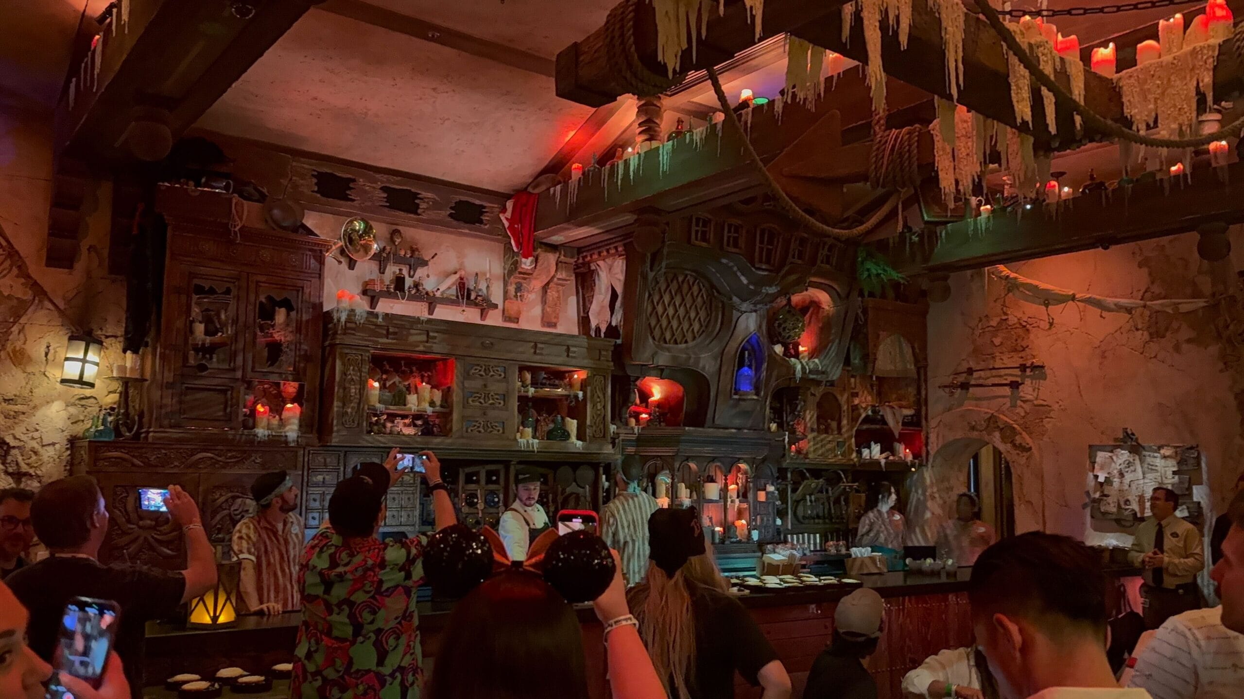 Dimly lit Beak and Barrel tavern with guests snapping photos of a costumed bartender behind an ornate Pirates of the Caribbean bar.