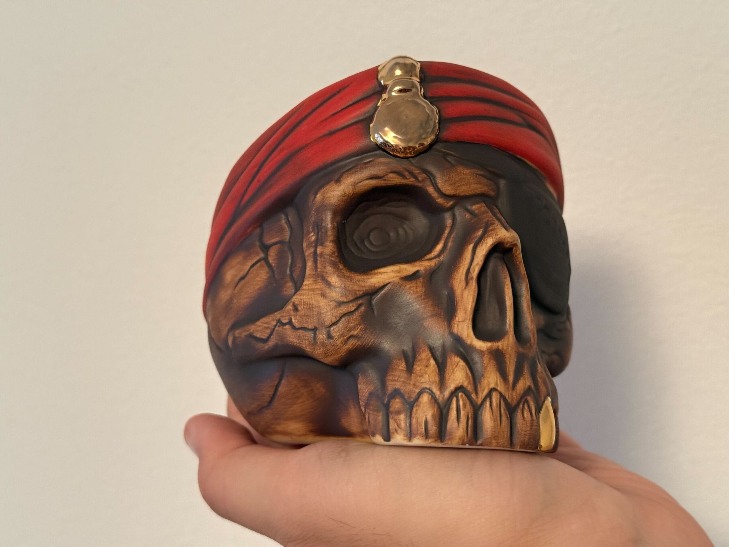 A hand holds the First Edition Pirate Skull Mug, featuring a red turban and gold ornament, against a plain background.