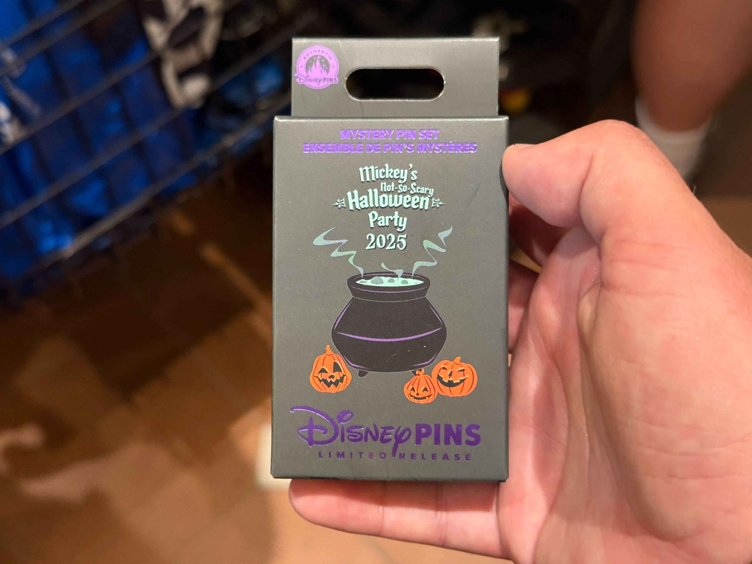 Hand holding 2025 merchandise pin box for Mickey’s Not So Scary Halloween Party, featuring a cauldron and pumpkins.