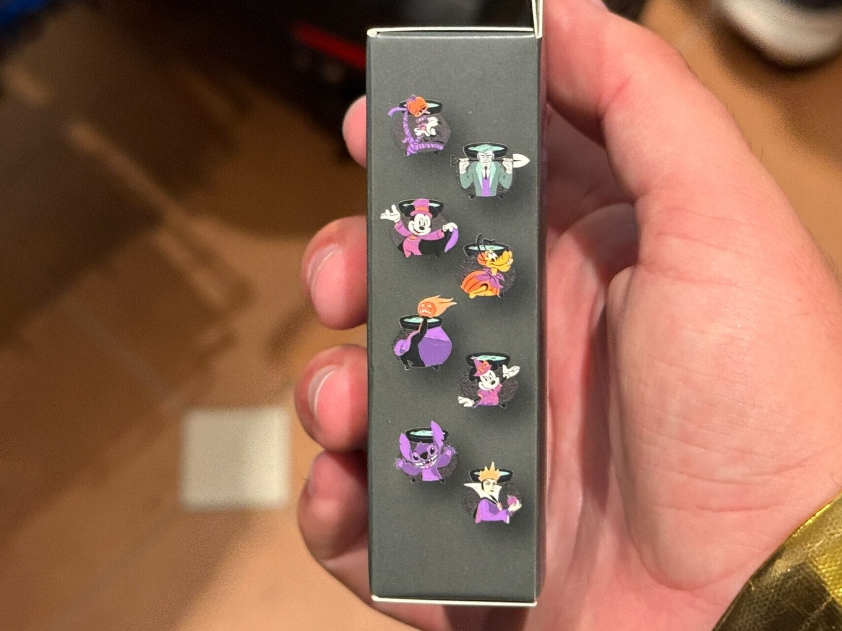 A hand holds a box displaying nine small, colorful Pokémon pins—perfect for 2025 merchandise collectors.