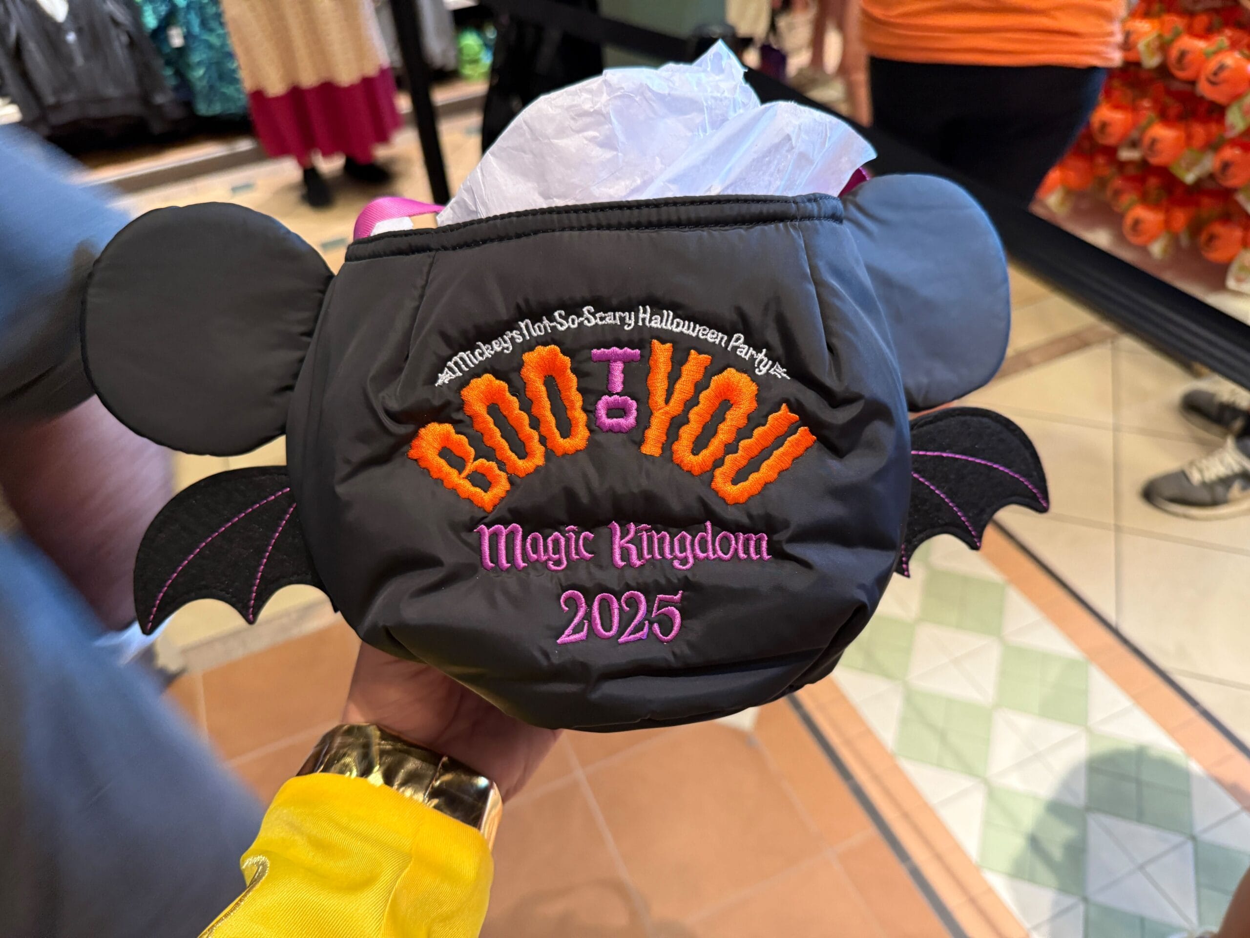 A hand holds 2025 Mickey's Not So Scary Halloween Party Merchandise: a Mickey ear bat wing bag embroidered with "Boo To You.