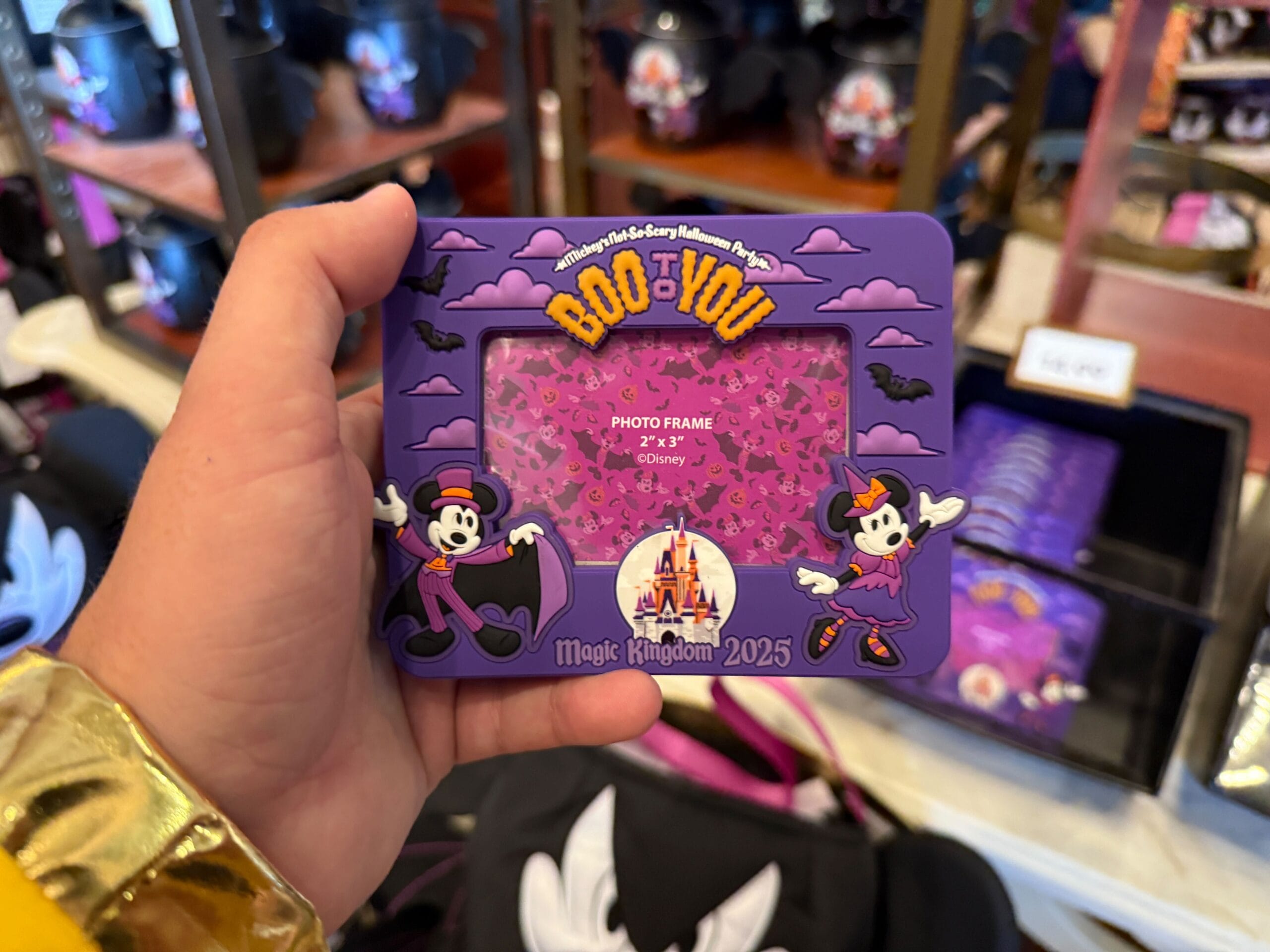 A hand holds a 2025 "Boo To You" frame—Mickey’s Not So Scary Halloween Party merchandise with Mickey and Minnie.