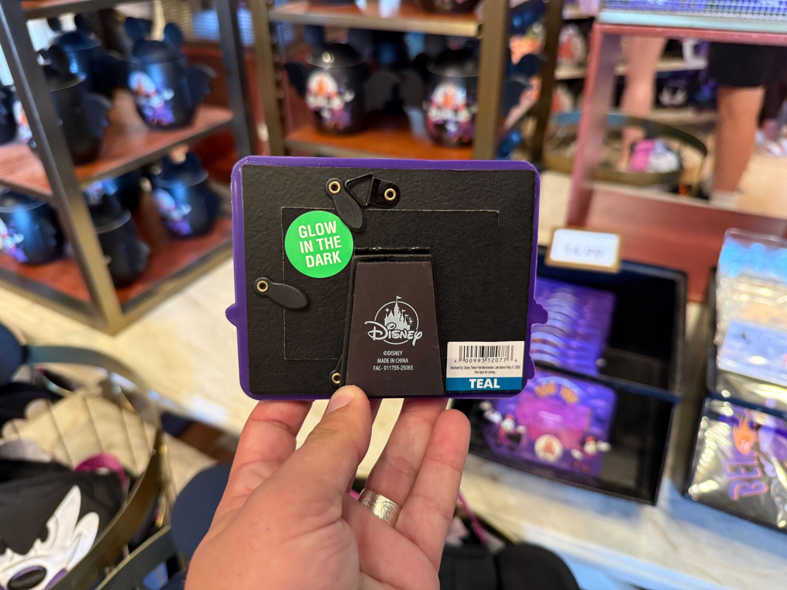 A hand holds a Disney photo frame with a "Glow in the Dark" sticker among 2025 merchandise in the store.