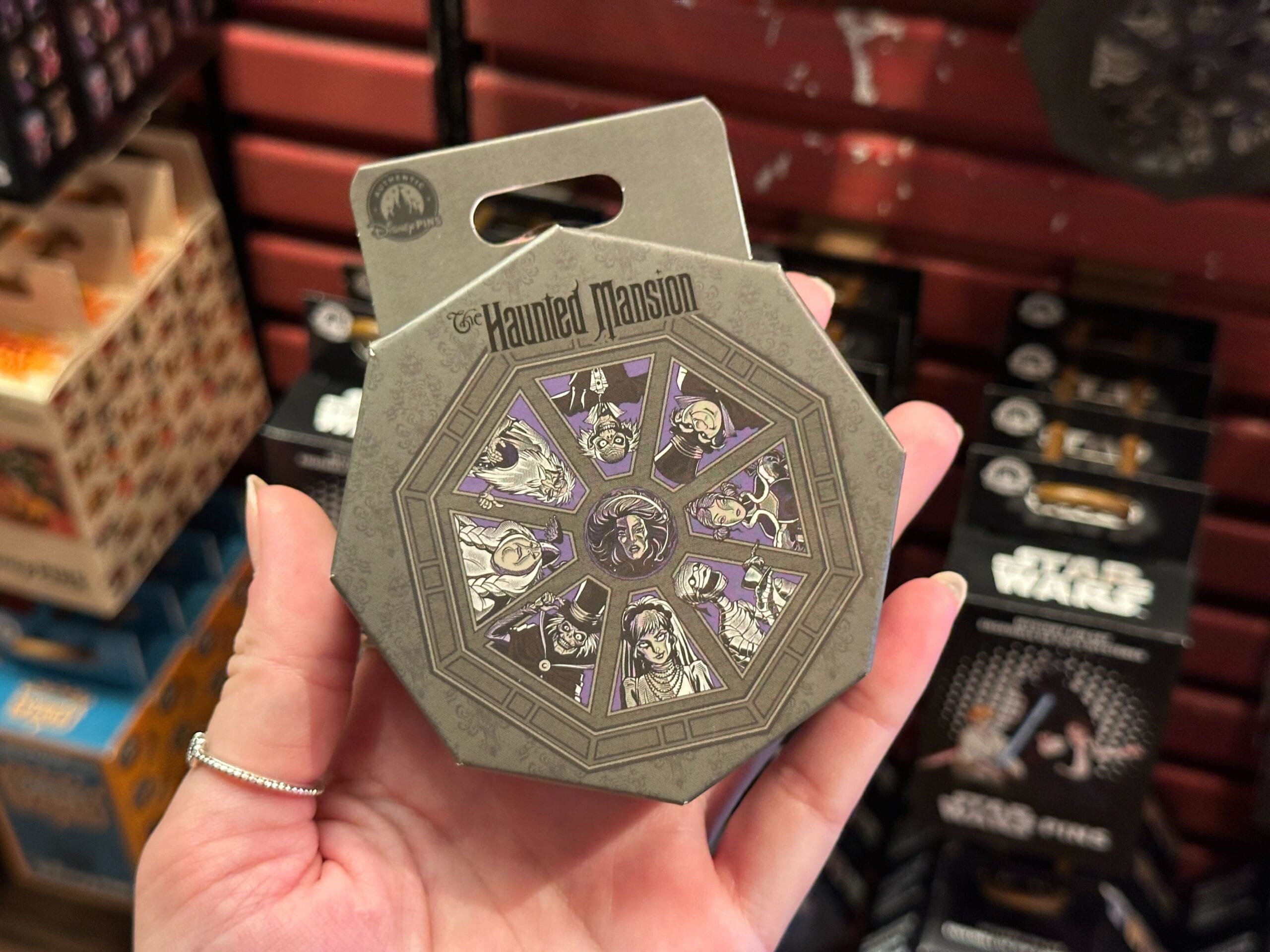 A hand holds a Haunted Mansion-themed souvenir with illustrated ghostly characters in a circular design.