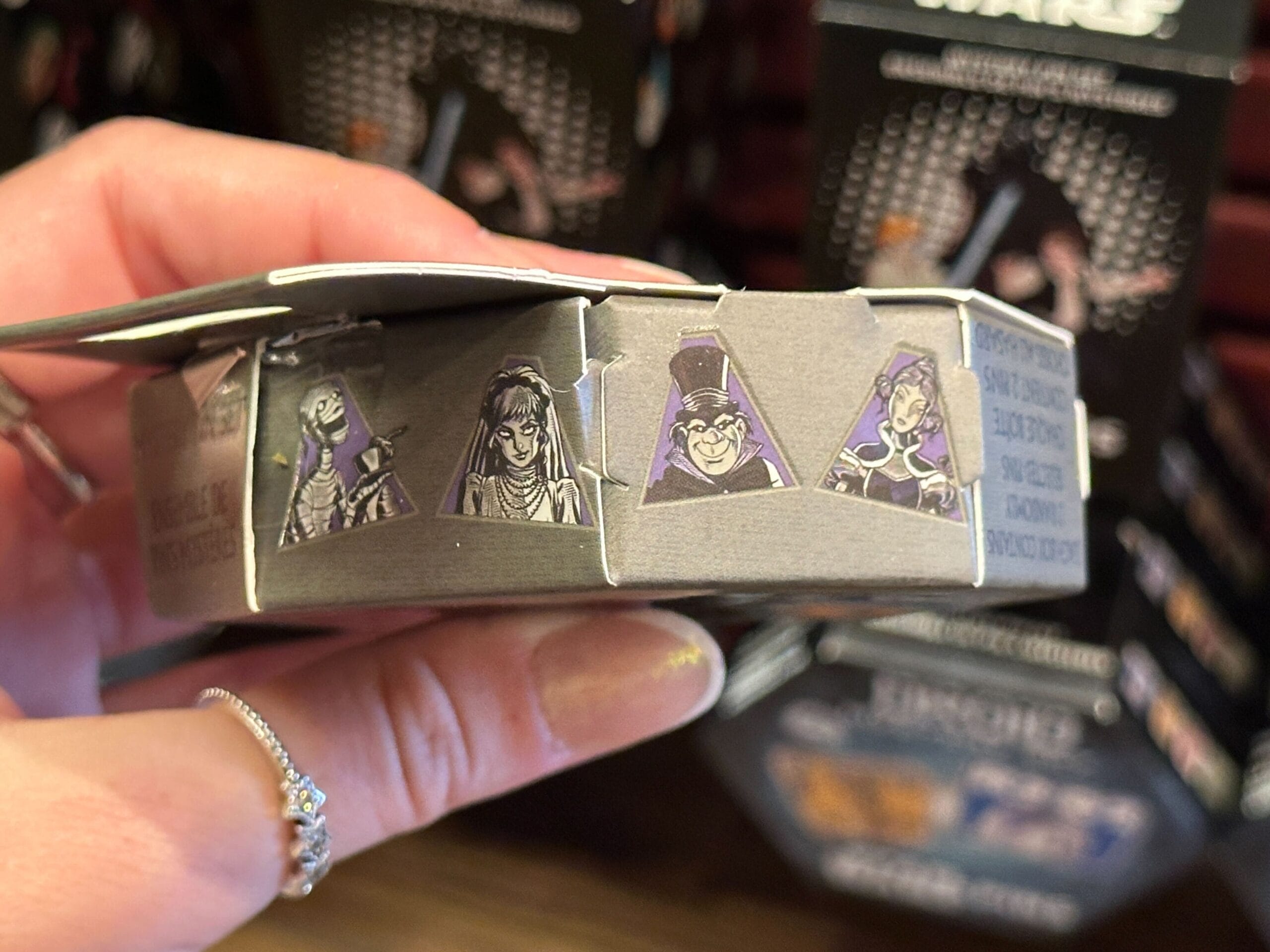 A hand holds a Mystery Pin box featuring illustrated Disney villains in purple triangles on the side.